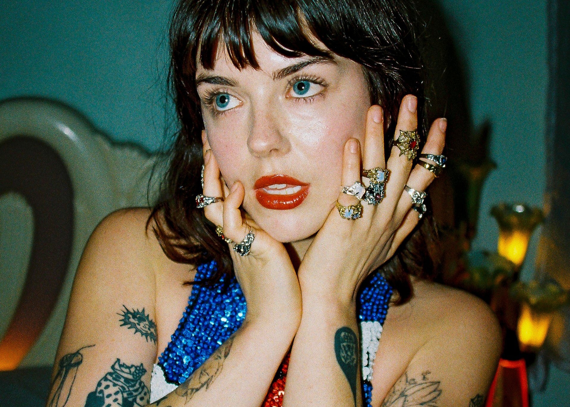 Woman with tattoos and jewelry posing in a colorful dress.