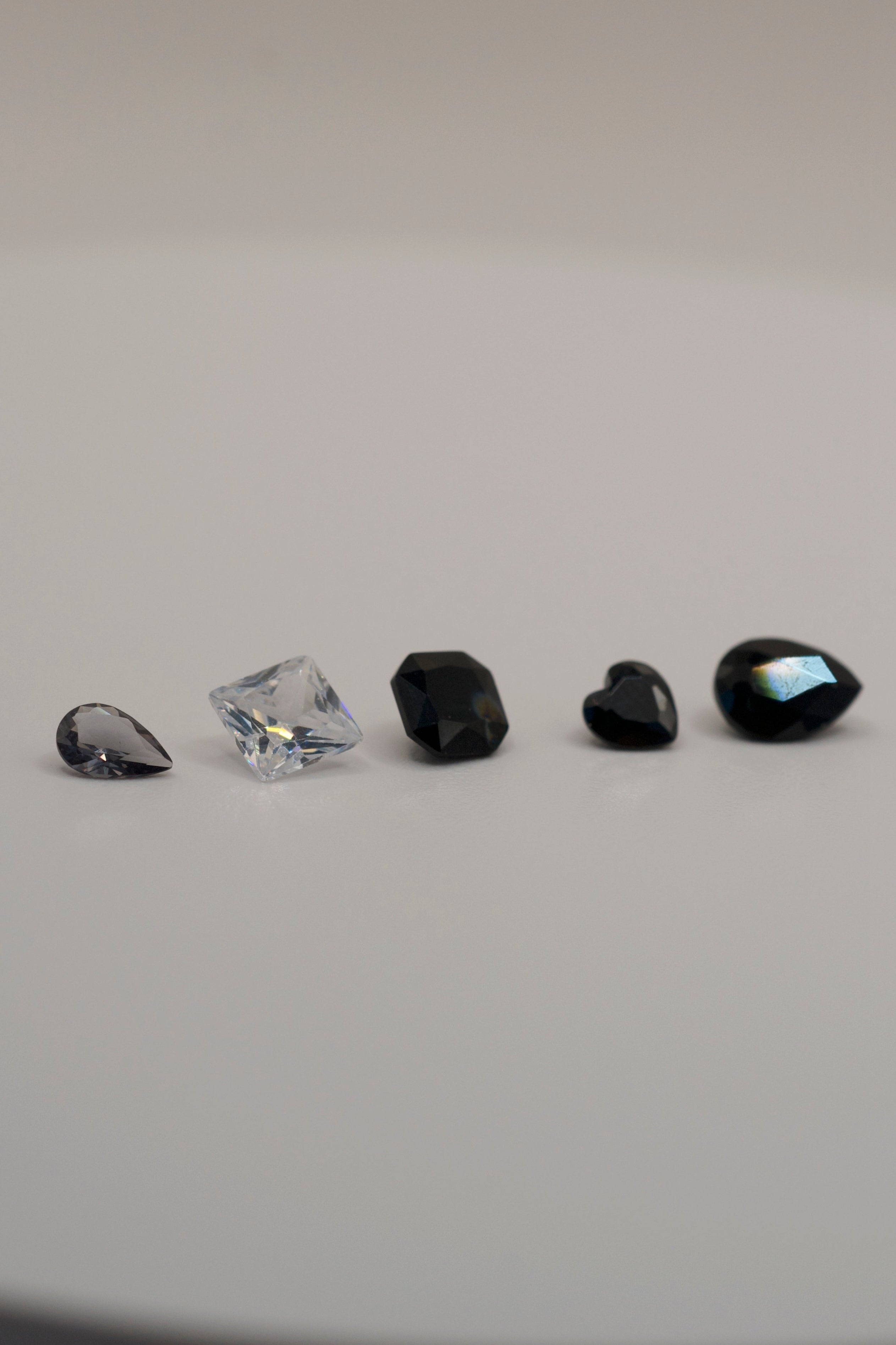 Gemstones for cast in place wax carving jewellery — black and clear faceted stones in pear, heart, cushion, and princess cuts on white background.