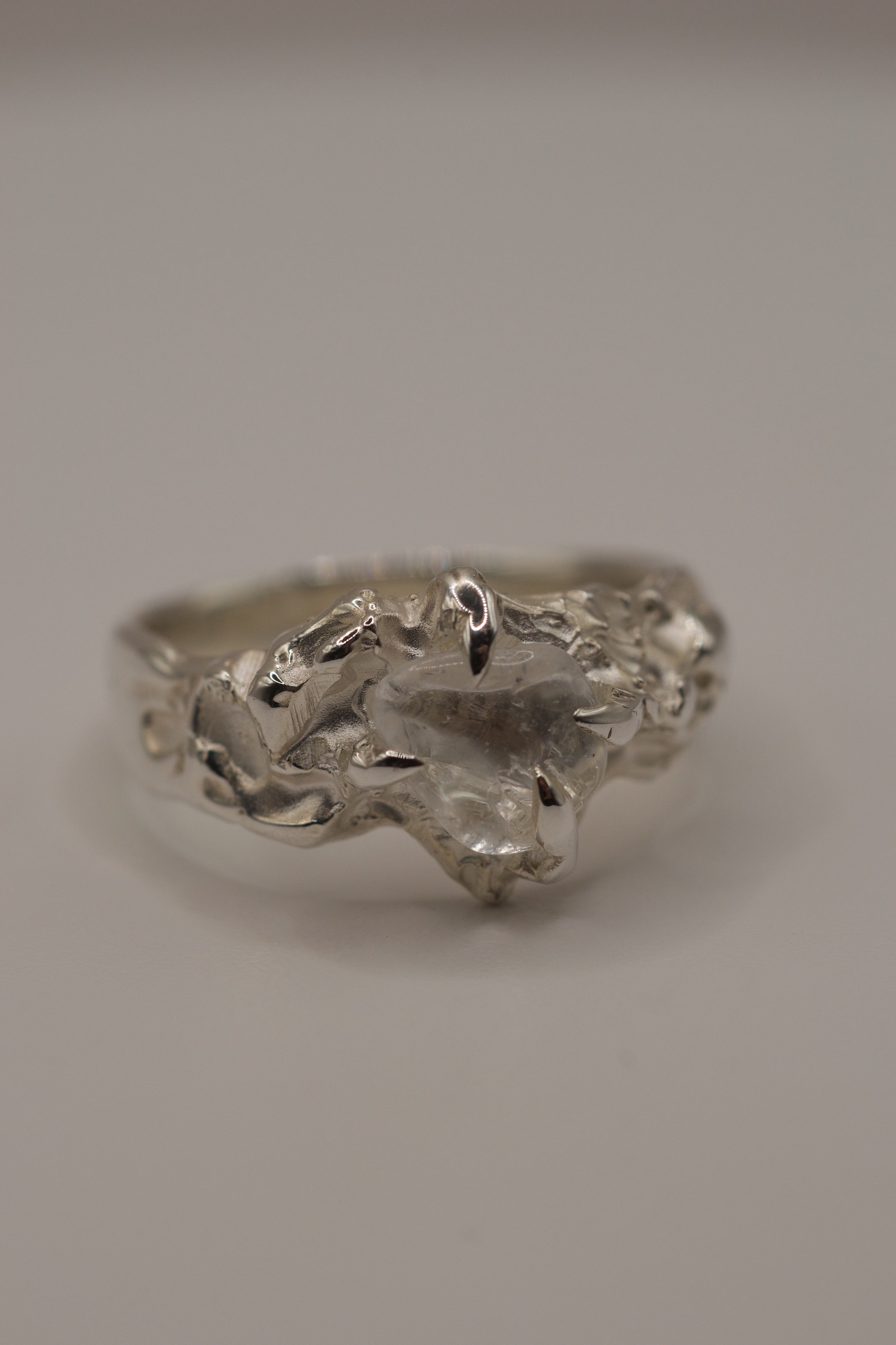 Unique handmade sterling silver ring with raw clear quartz crystal, organic molten claws holding stone, front view highlighting gemstone shape.