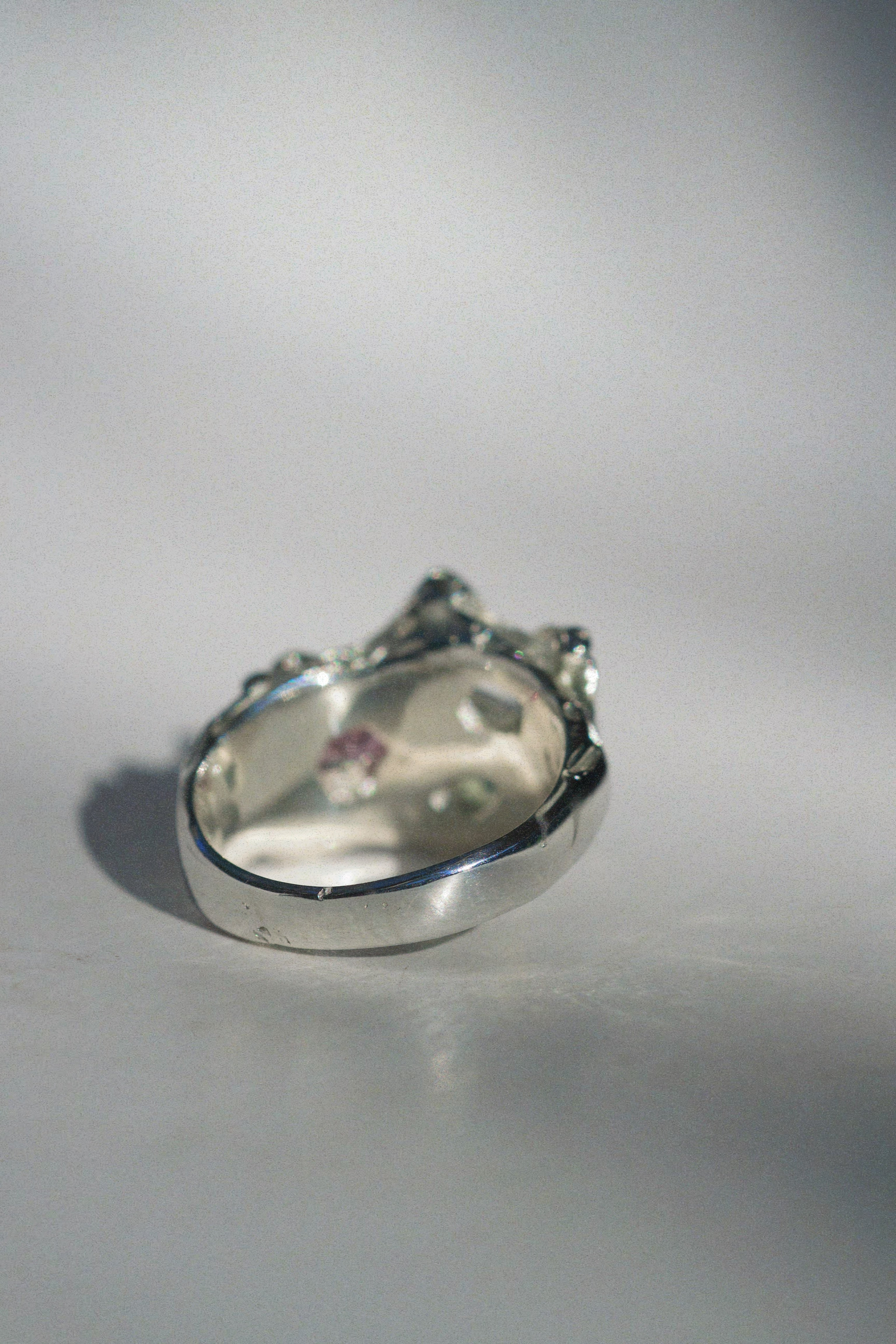 Back angle view of a handmade silver ring with an organic cluster gemstone layout. Features emerald-cut white sapphire, pink cushion-cut CZ, and aqua opal nestled in textured silver that resembles a wildflower in bloom, cast using the lost wax process.