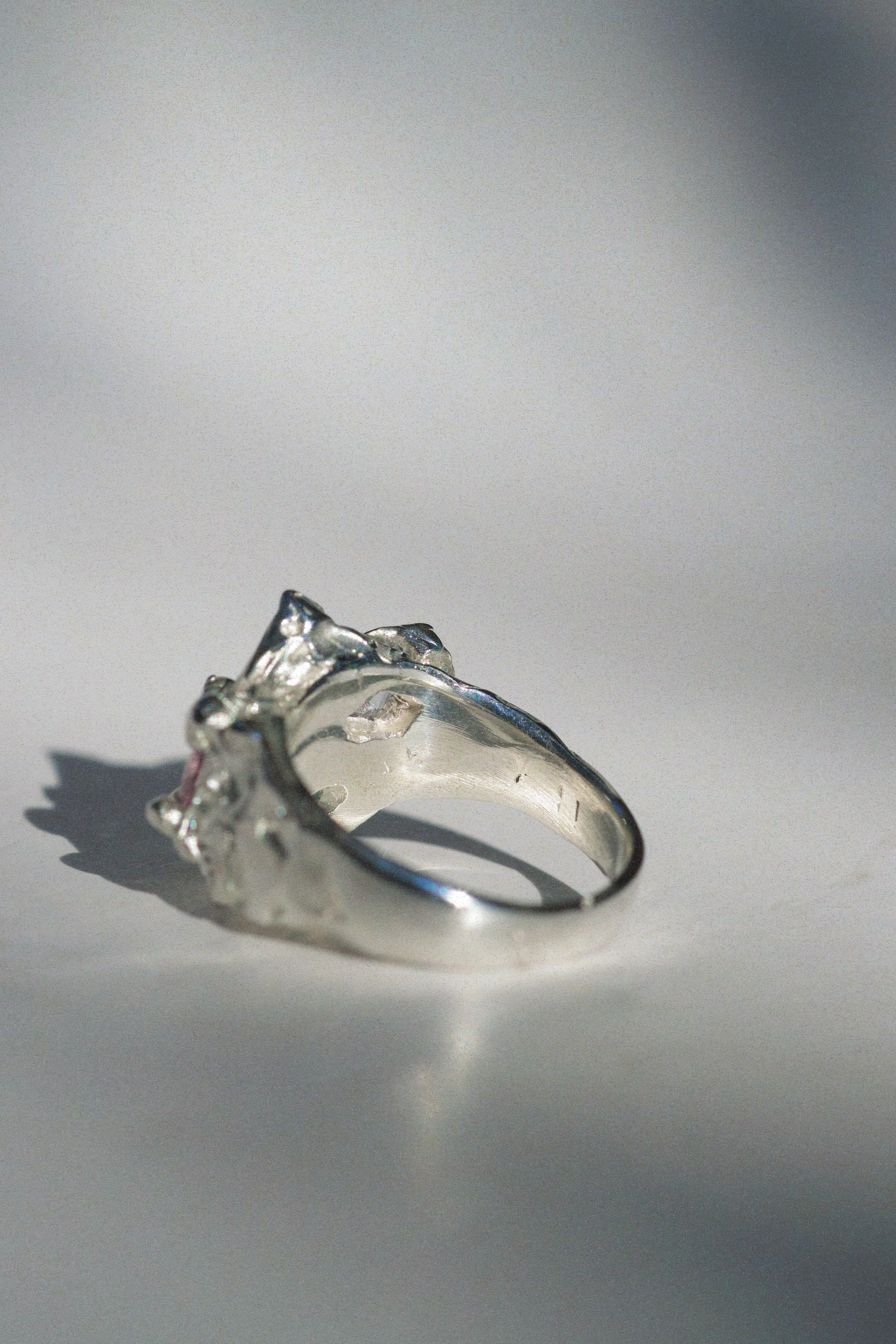 Macro shot of the fantasy silver ring’s molten band and detailed cluster setting. The gemstones — emerald-cut white sapphire, pink cushion-cut cubic zirconia, and round aqua opal — are surrounded by raw, sculpted textures created through traditional lost wax casting.