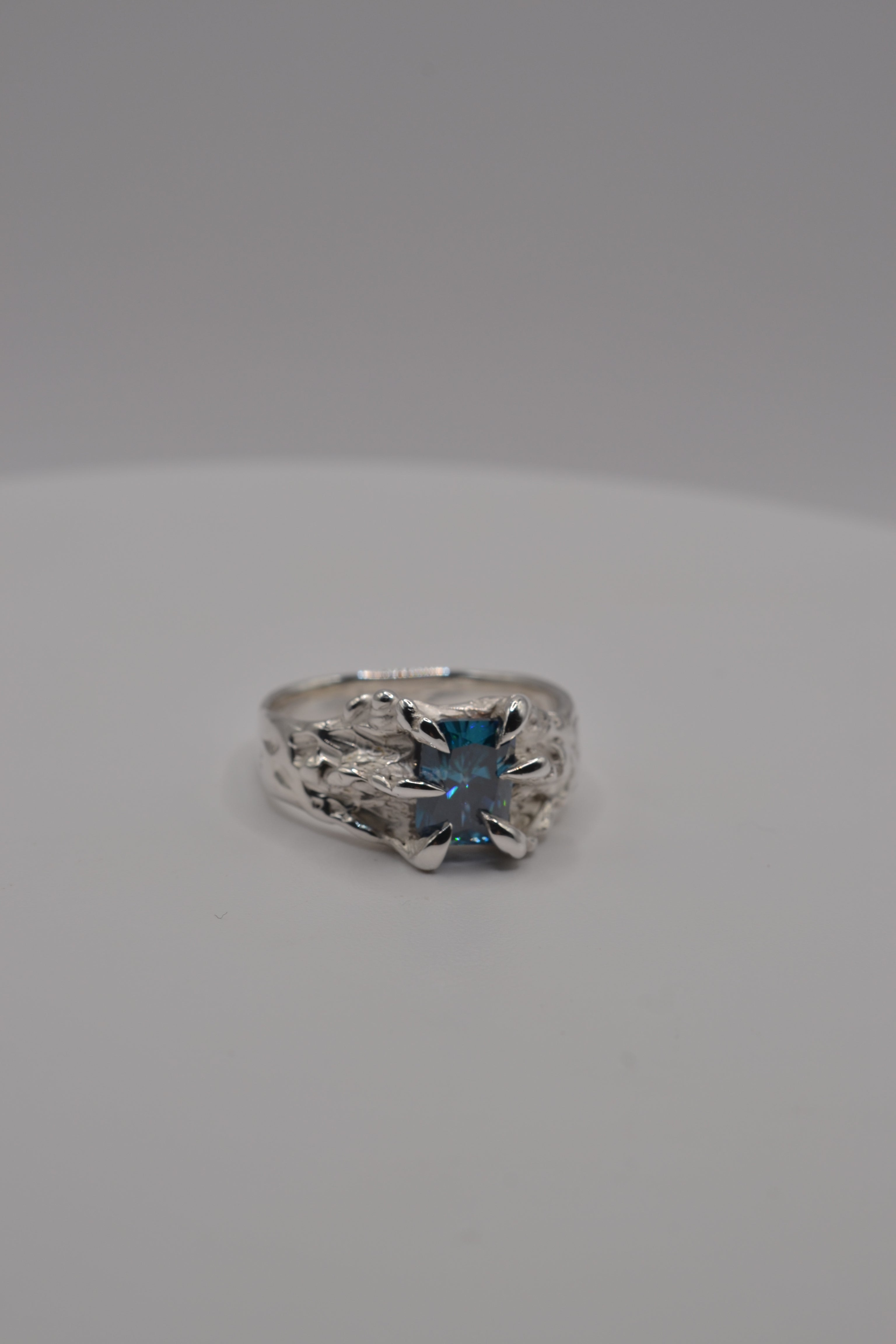 Front-facing view of a handmade lost wax silver ring featuring a blue radiant cut moissanite in an organic setting.