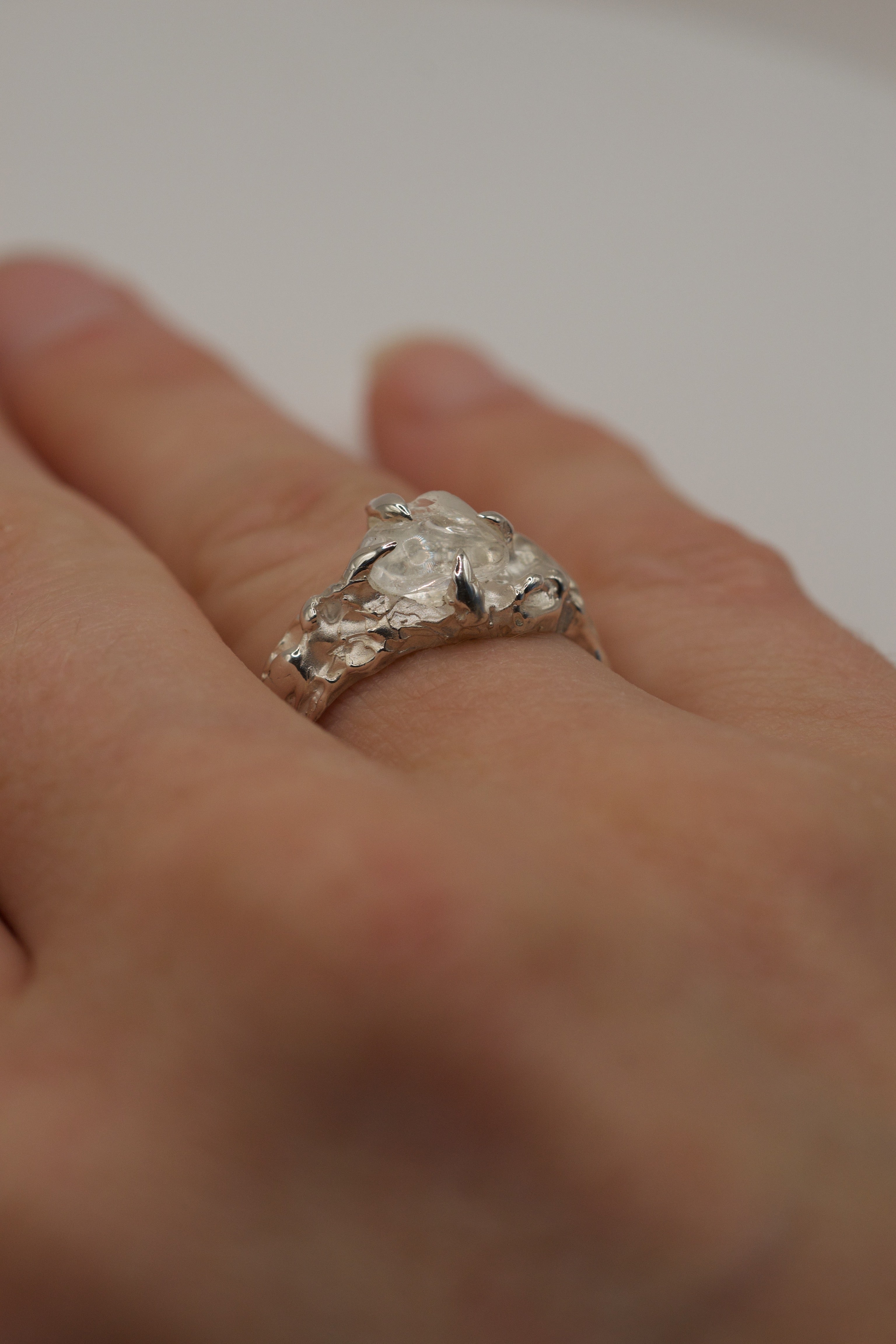 Close-up of handmade lost wax sterling silver ring worn on hand, organic molten band with raw clear quartz crystal.
