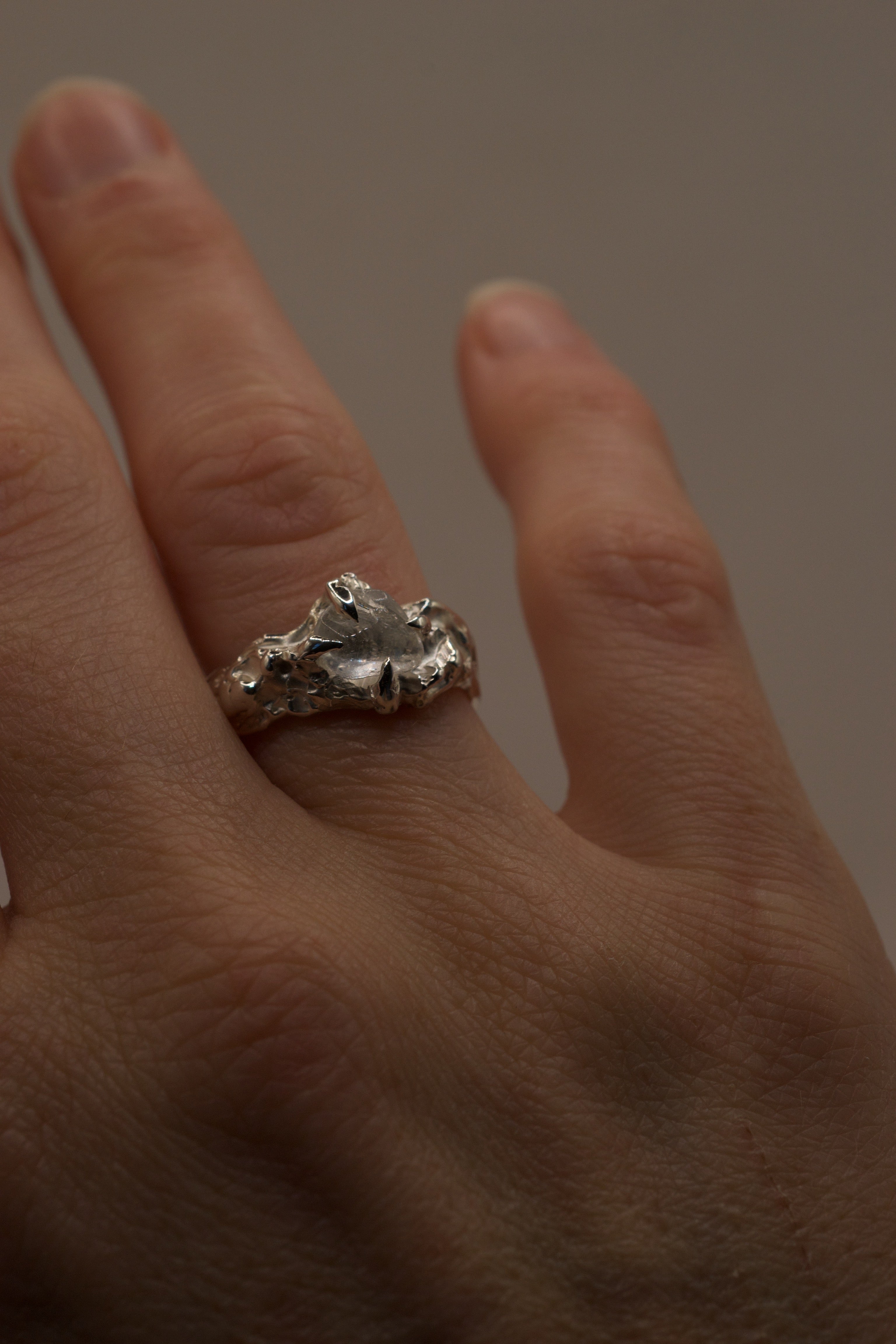 Handmade lost wax sterling silver ring with molten organic claws holding irregular clear quartz, side angle view on hand.