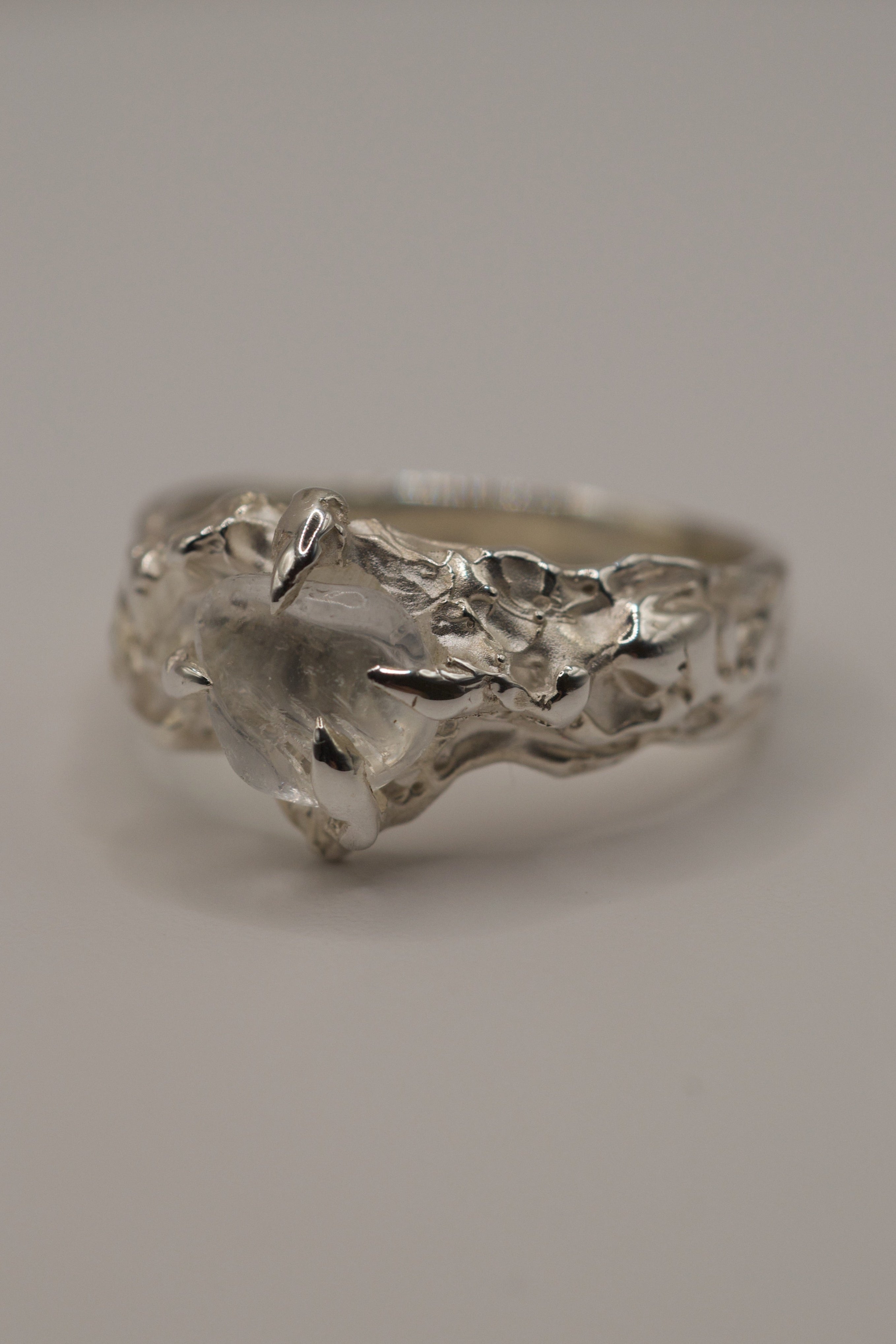 Handmade lost wax sterling silver ring with molten organic band, irregular clear quartz gemstone, angled detail view.