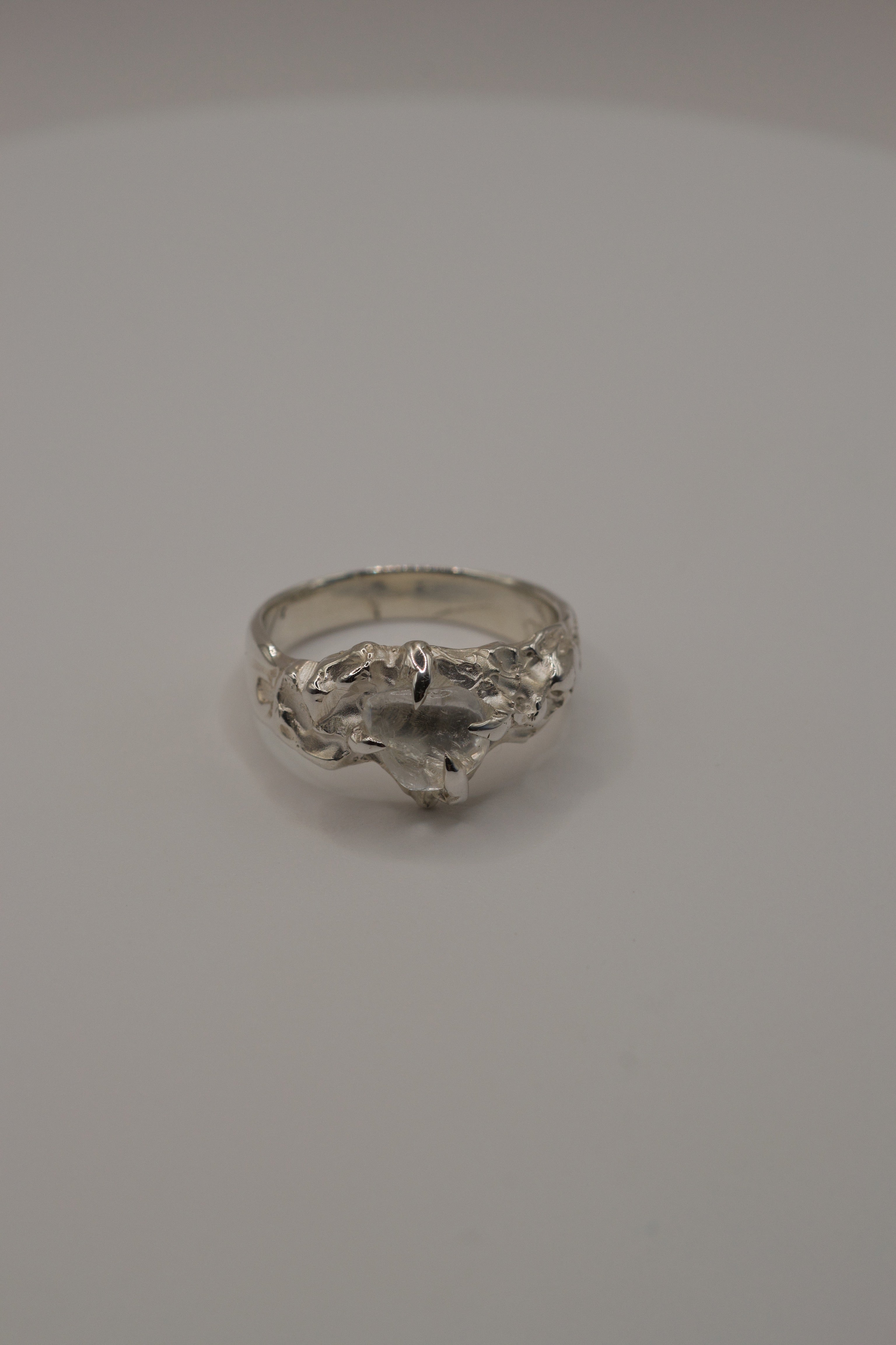 Overhead shot of handmade lost wax sterling silver ring, organic molten band holding irregular clear quartz crystal.