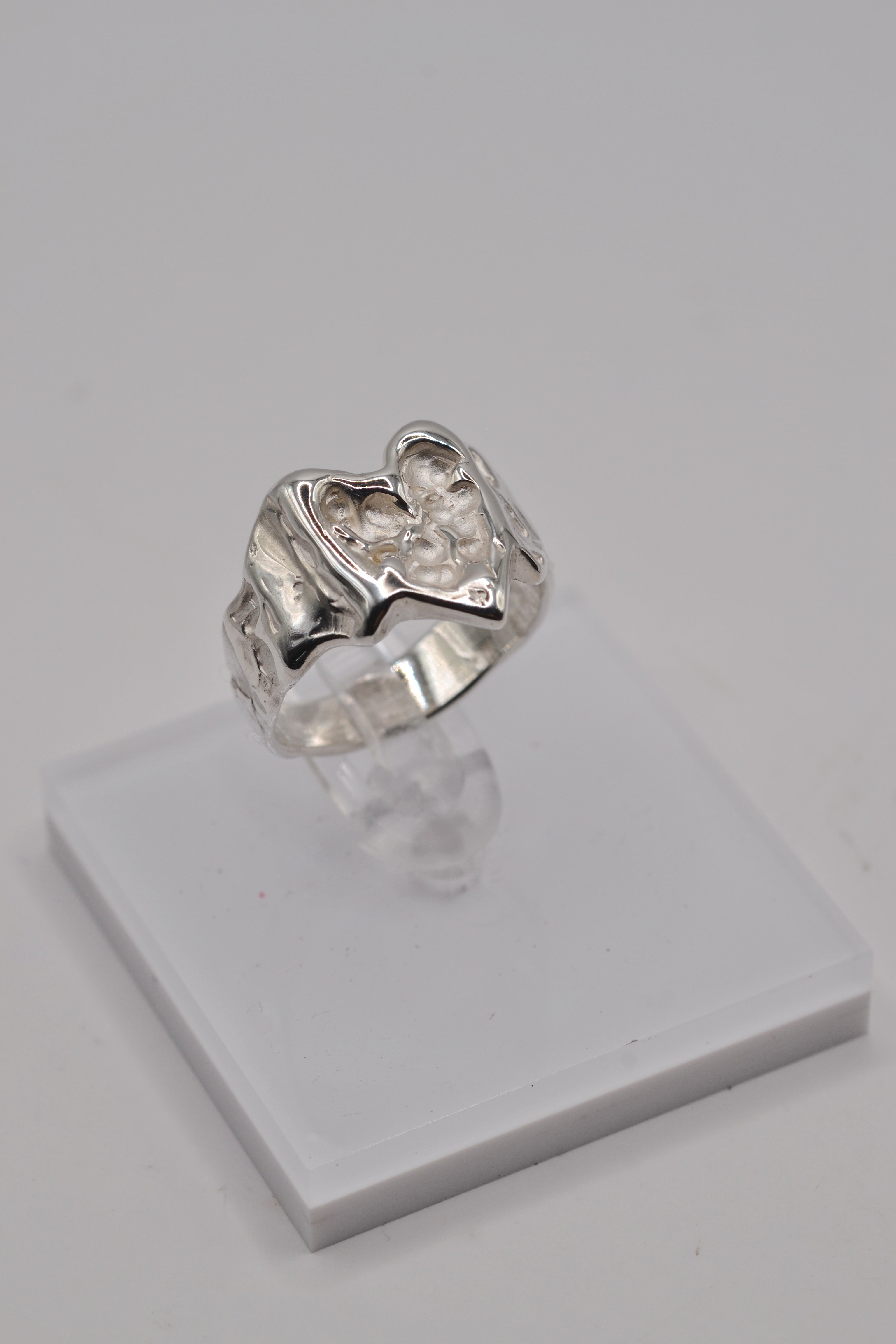 Organic lost wax cast ring displayed on clear stand, sterling silver handmade heart ring from side angle left view