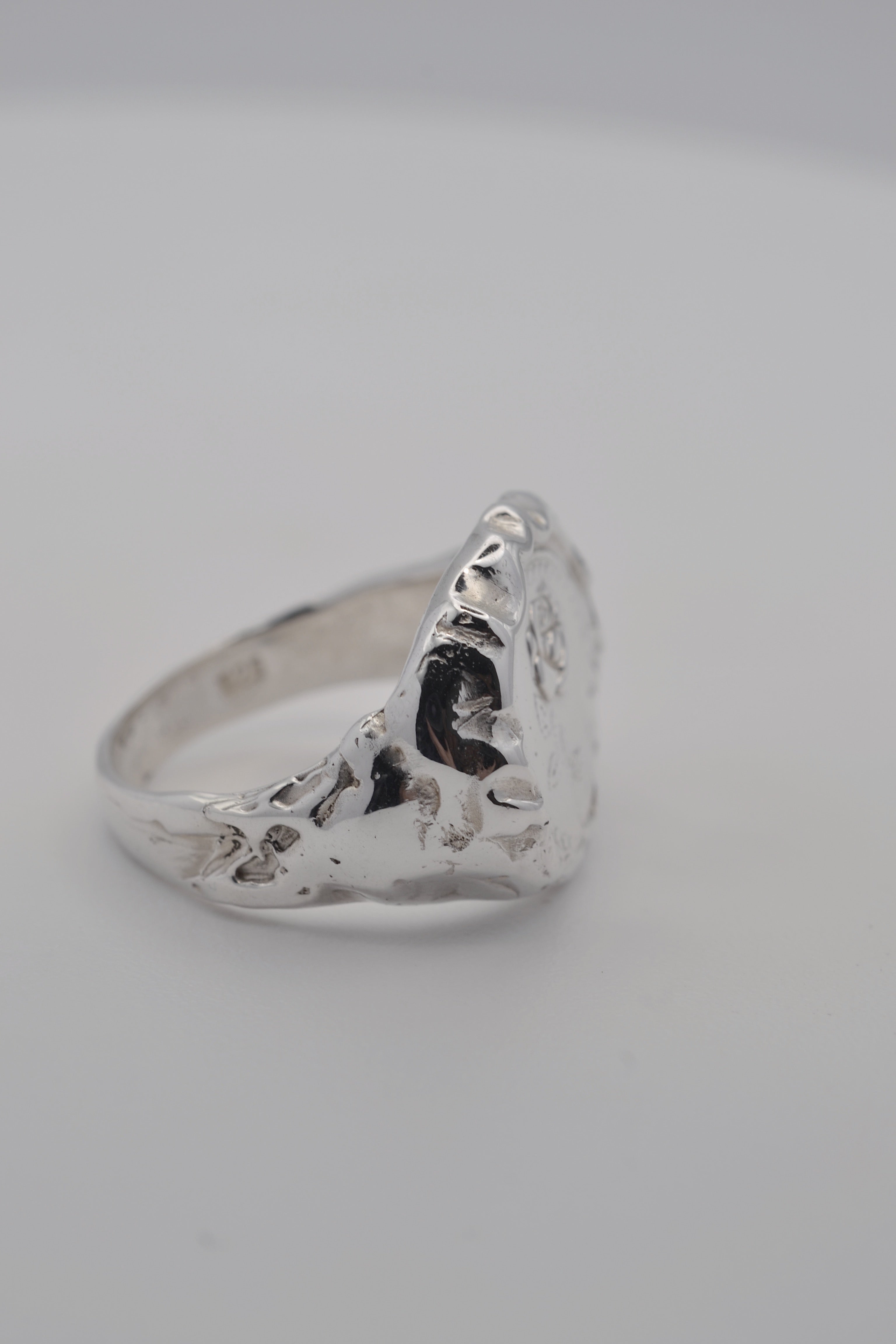 Handmade lost wax silver ring with sculptural molten edges and a raised embossed rose design, photographed during finishing.