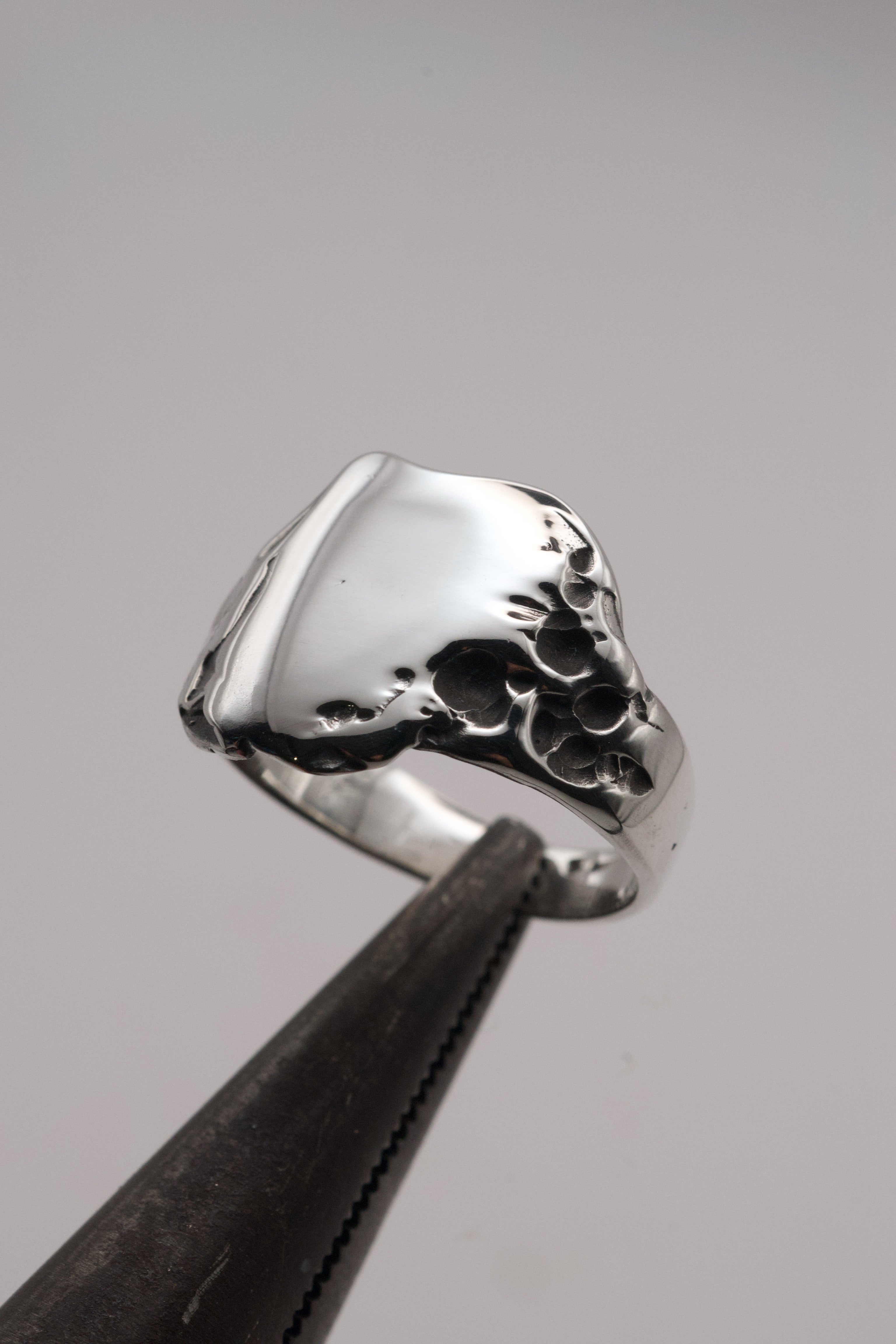 A macro close-up of the handcrafted sterling silver signet ring, showing crater-like molten details and smooth polished surface created using the lost wax technique.