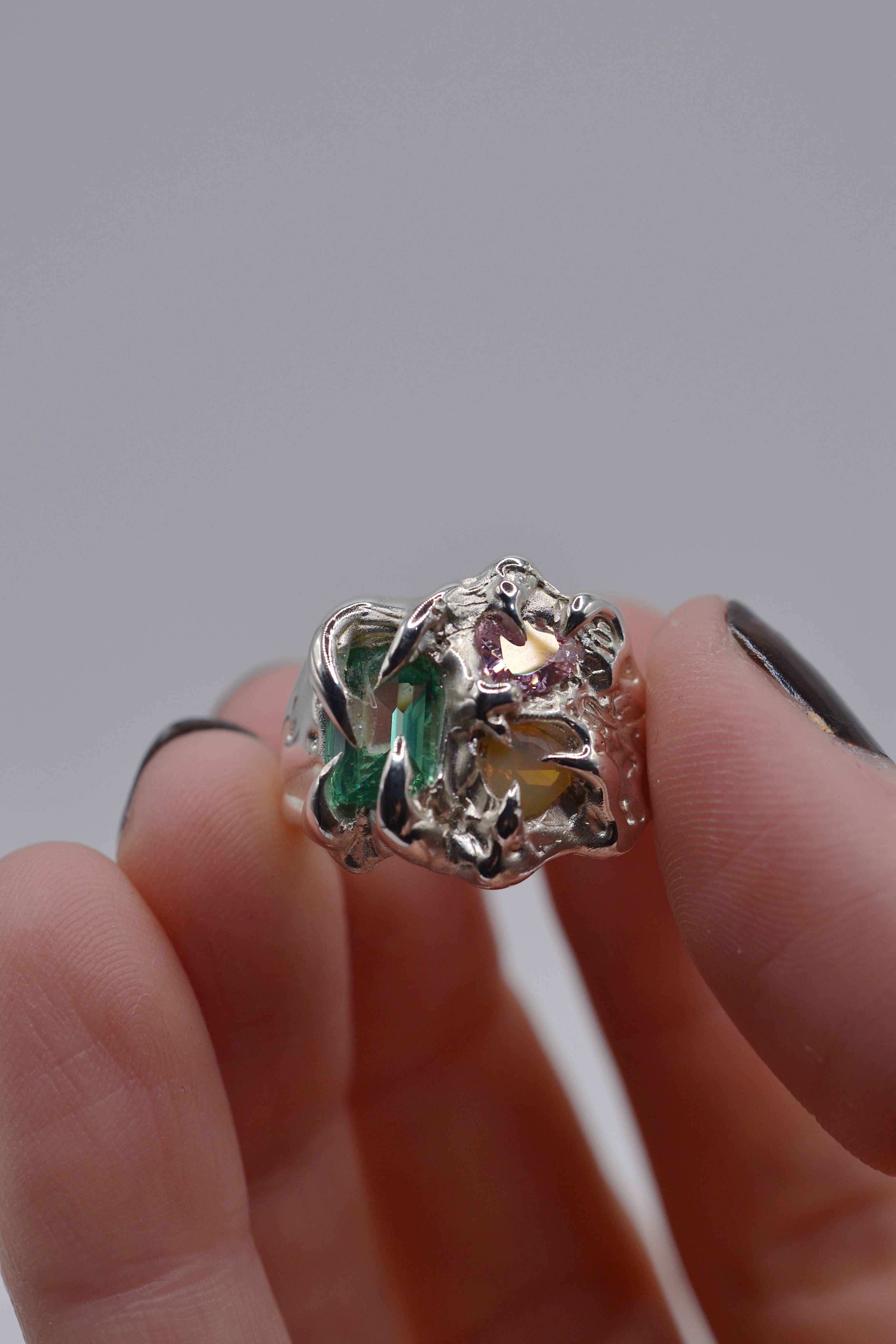 The Mirage ring held. Handmade organic silver, wax carved and lost wax cast. Set with green tourmaline, pink heart CZ and yellow opal. Metal Bones Jewellery.