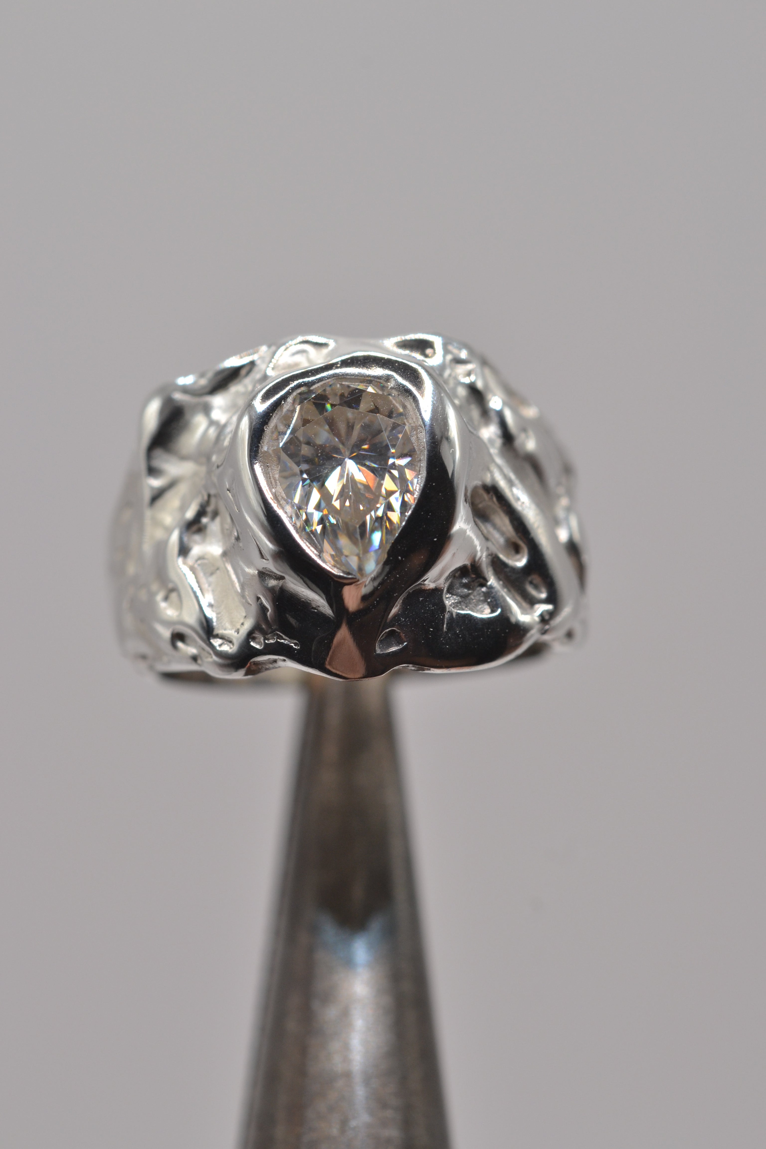 The molten silver moissanite ring displayed on jeweller’s pliers, highlighting the textured lost wax detailing and bold organic shape.