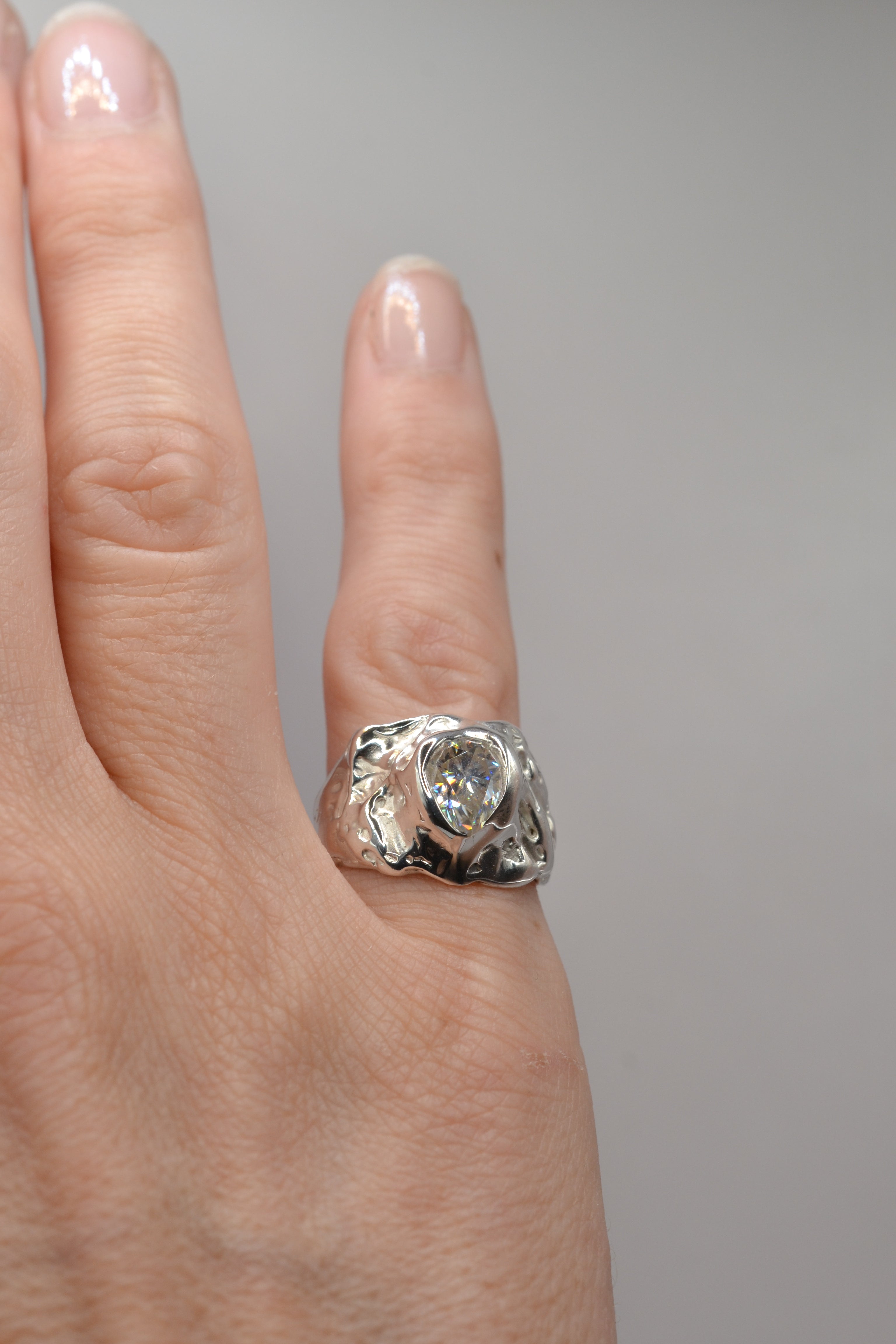 Close-up of the molten silver lost wax moissanite ring worn on the hand, showing fit, shine, and organic sculptural detail.