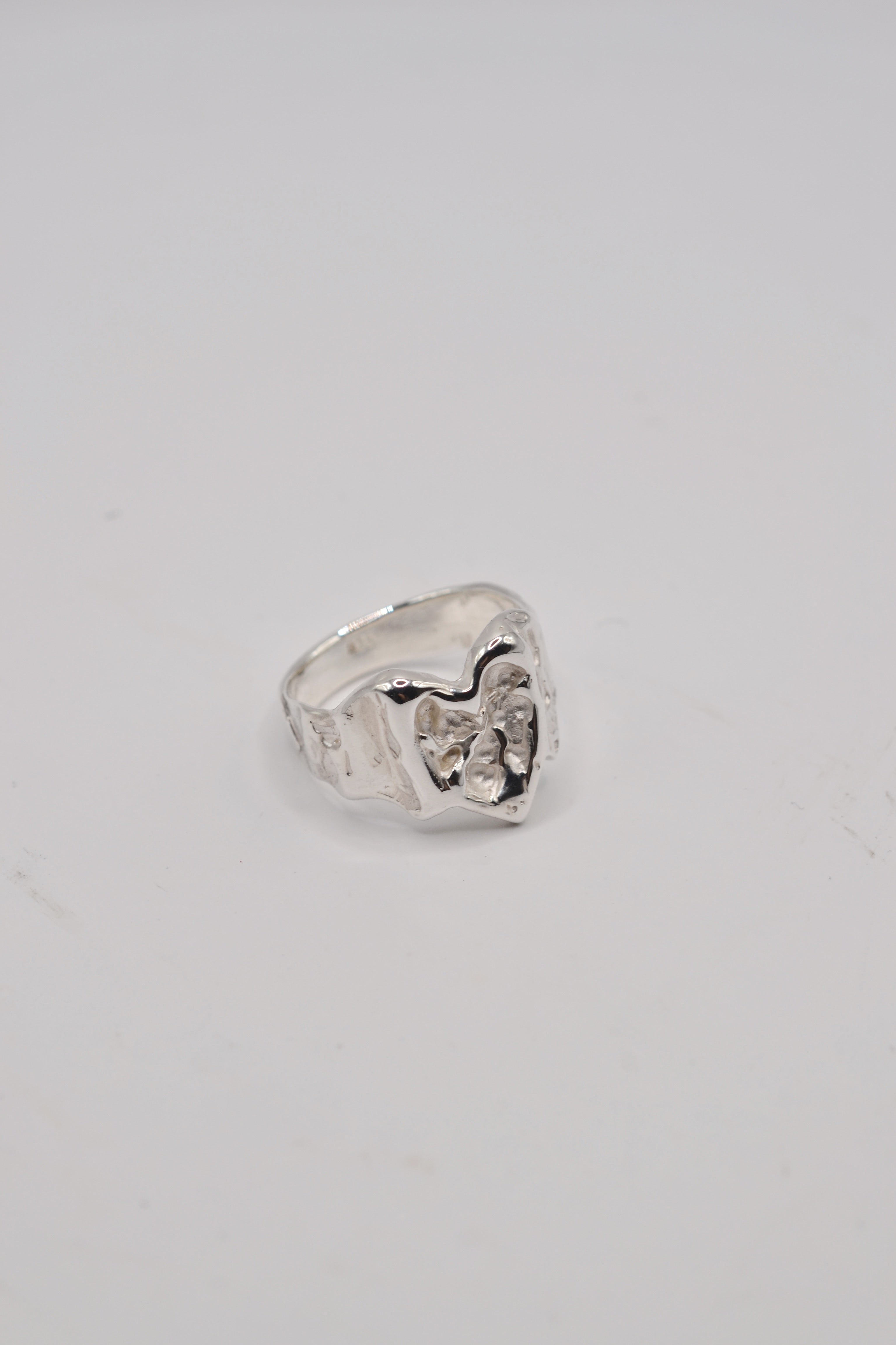 Angled close up of organic lost wax cast ring in sterling silver highlighting molten heart jewellery design