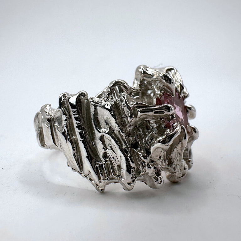 Silver ring made from molten metal with grooves and dimension, hand-carved using the lost wax method. This 925 sterling silver ring is centred with a light pink cushion crystal, showcasing a unique and textured design.