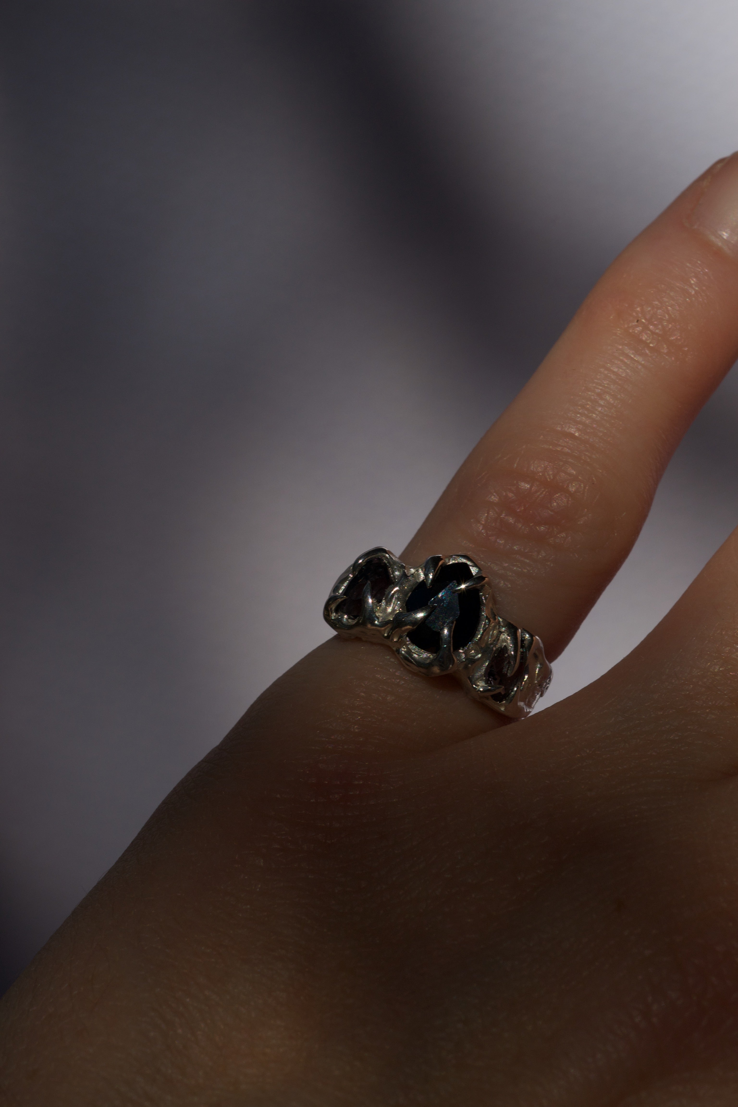 Close-up of a hand wearing a sterling silver handmade ring with black gemstones on a blurred background