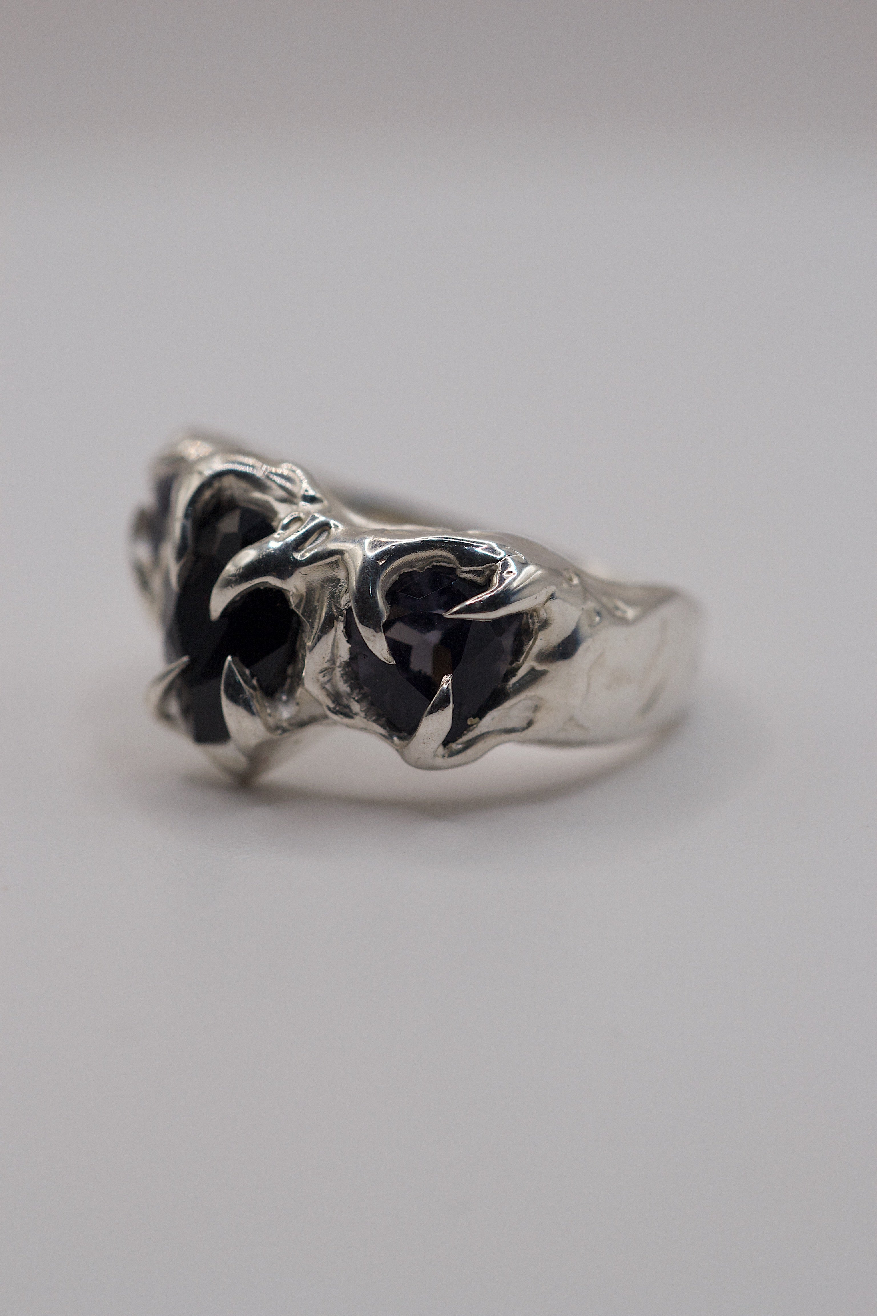 Side view of organic sterling silver handmade ring with gothic claws holding pear-cut lab-grown black and grey gemstones.
