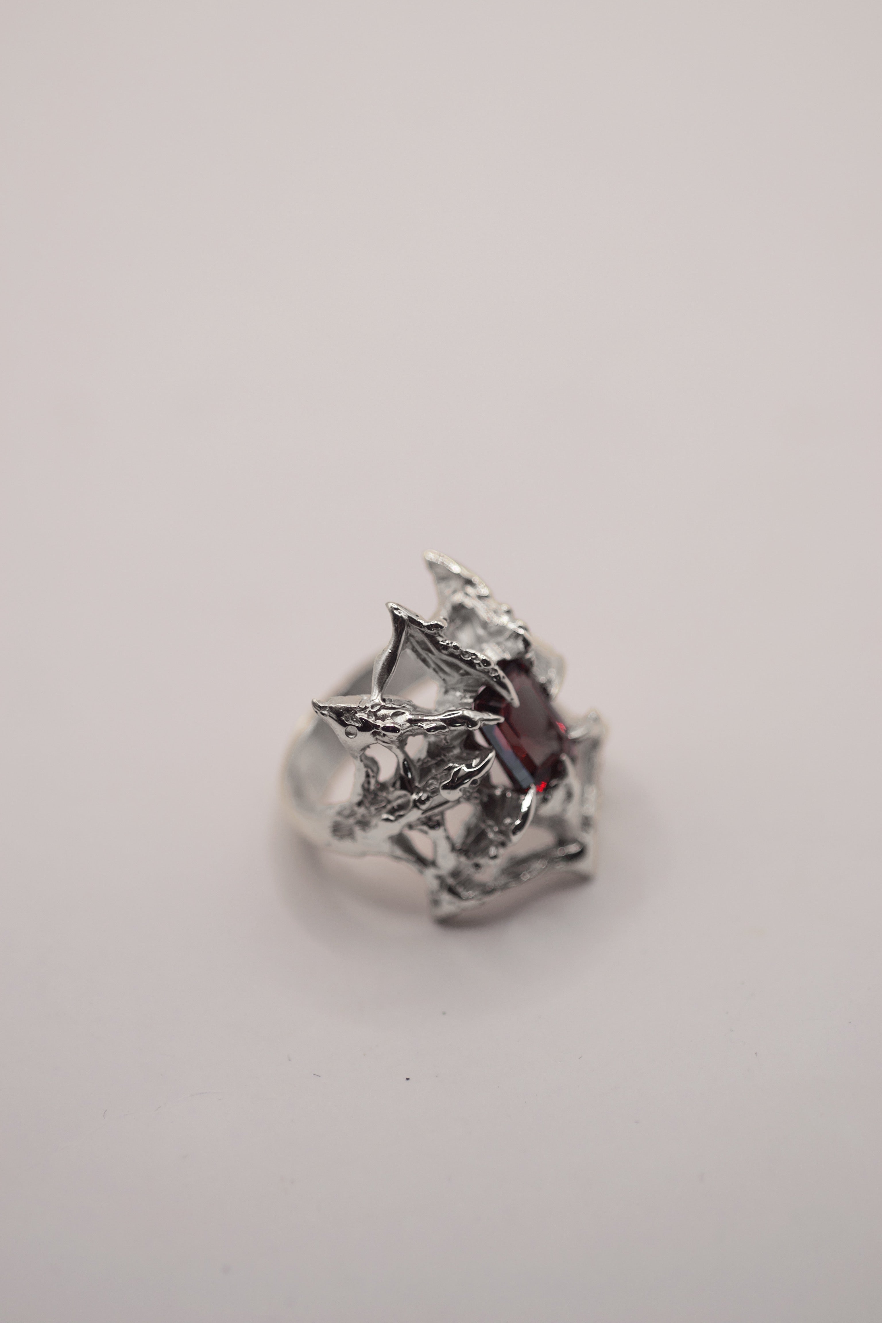 grunge gothic style lost wax cast sterling silver ring with a spider web holding a garnet emerald cut lab grown nano crystal. handcrafted using the lost wax method.