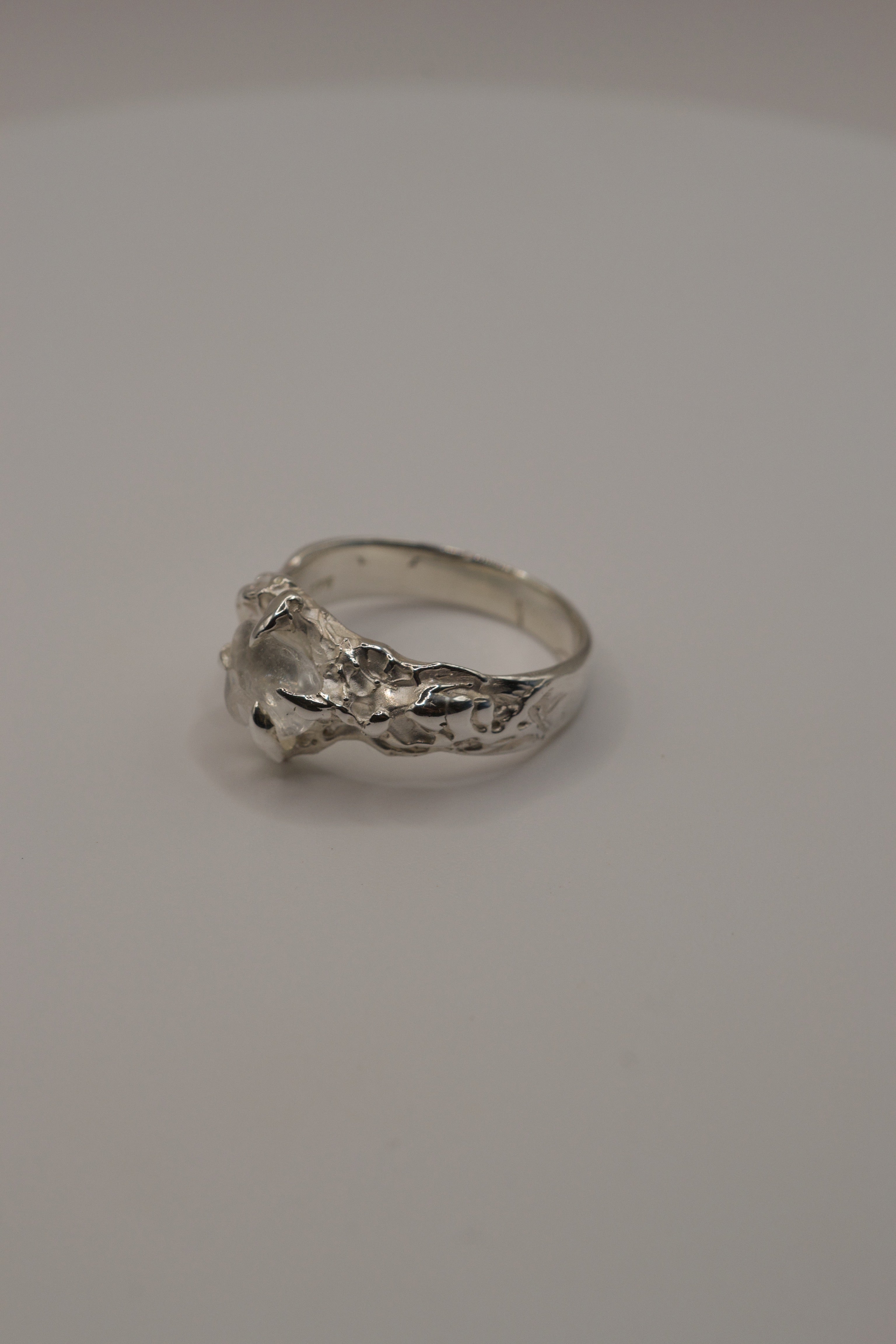 Handmade lost wax sterling silver ring with organic molten band and irregular clear quartz gemstone, angled display view.