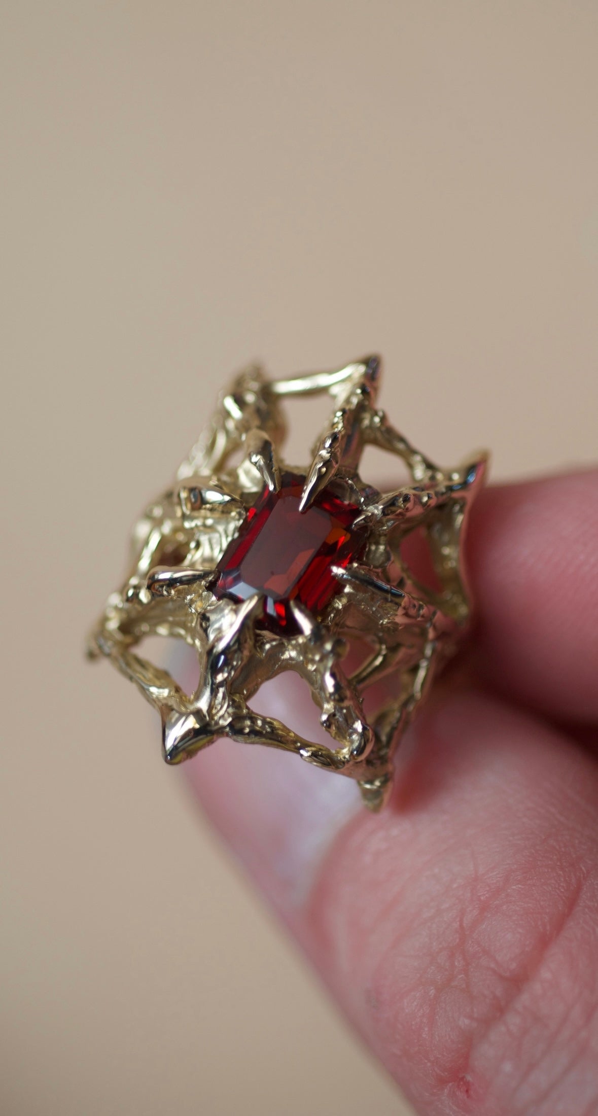 Lost wax cast gold Doom Ring worn on hand with intricate molten web structure and deep red garnet alternative sculptural jewellery