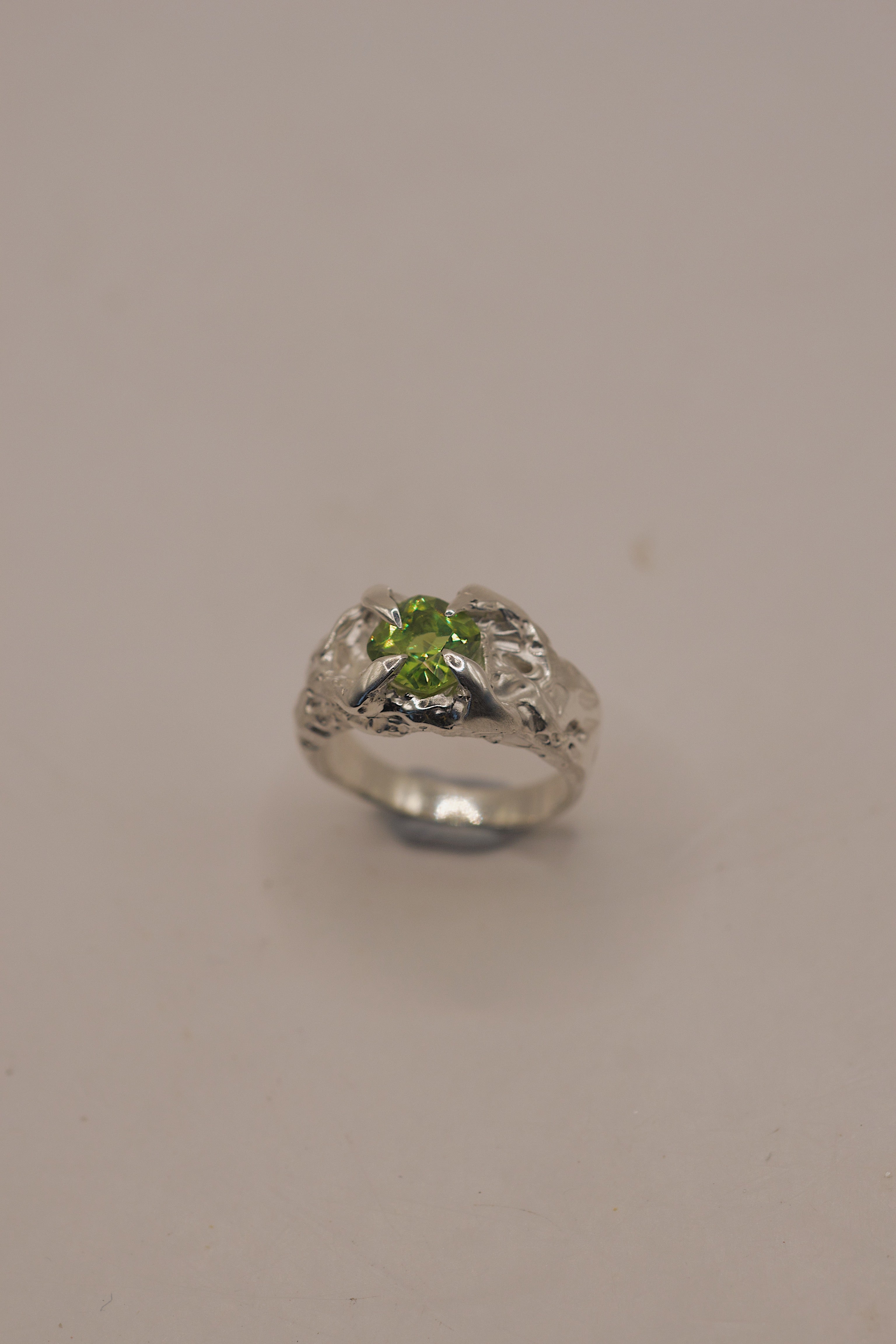 Flat view of the Fern Ring showing organic recycled sterling silver band with textured dimensional shoulders and green peridot setting