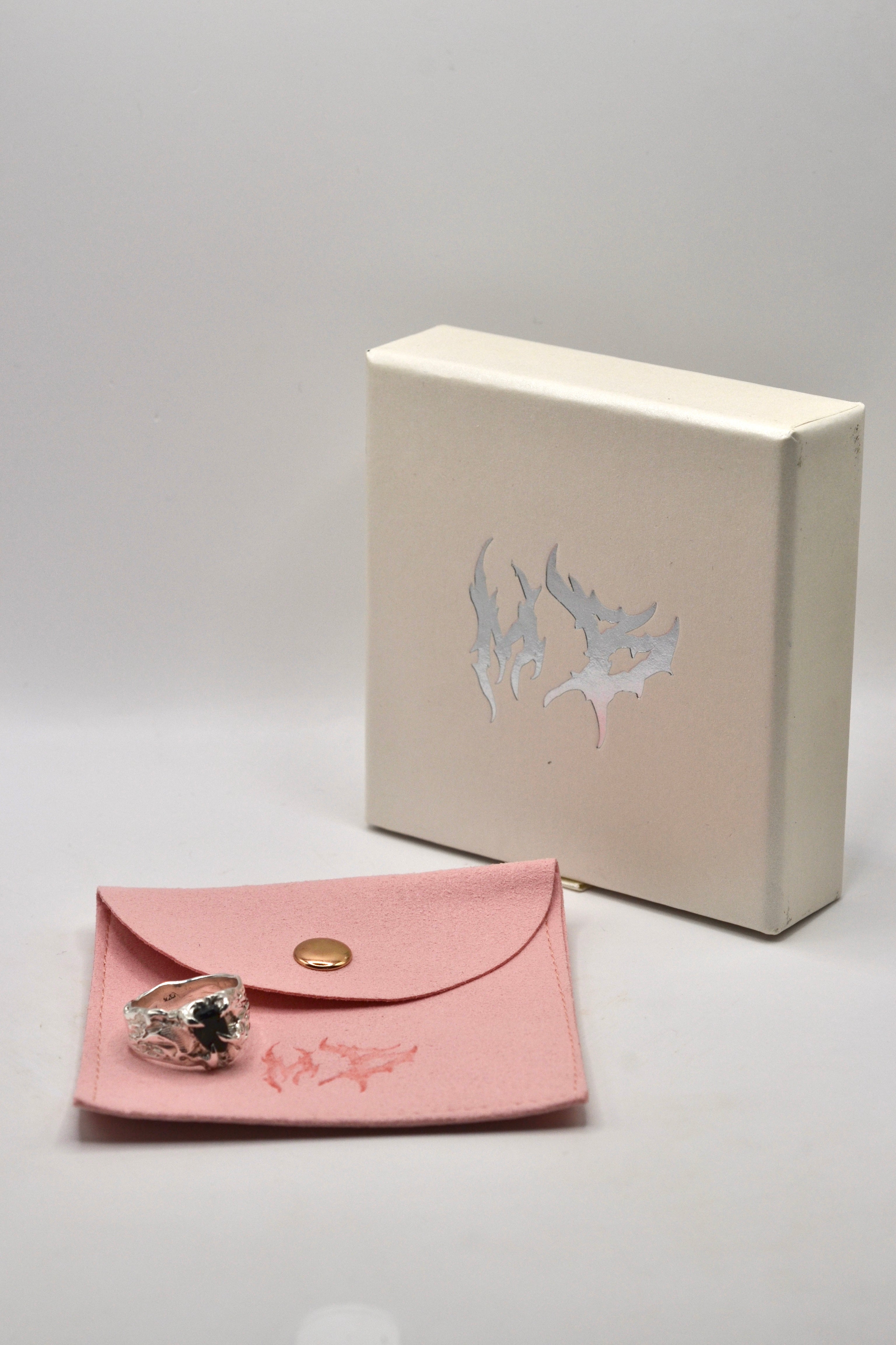 Pink jewellery pouch with an organic ring and a beige box on a white background