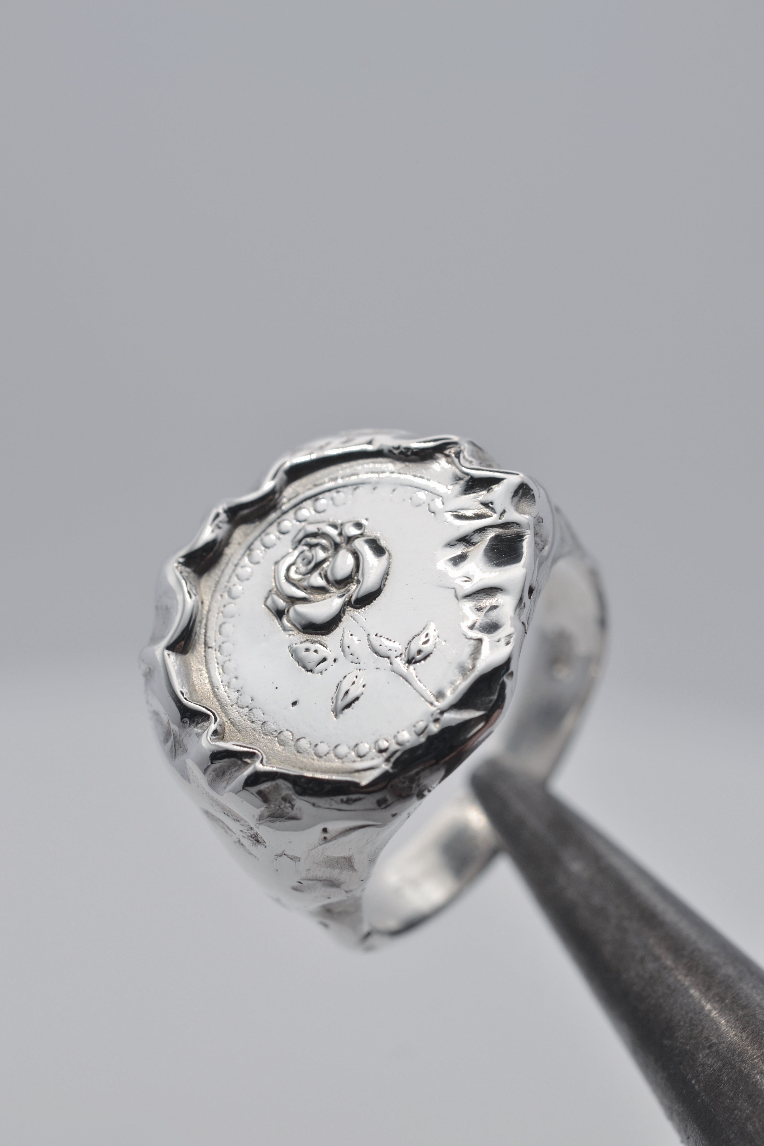 La Vie En Rose Ring held in tweezers showing embossed sterling silver rose surrounded by organic molten silver texture handmade using the lost wax technique