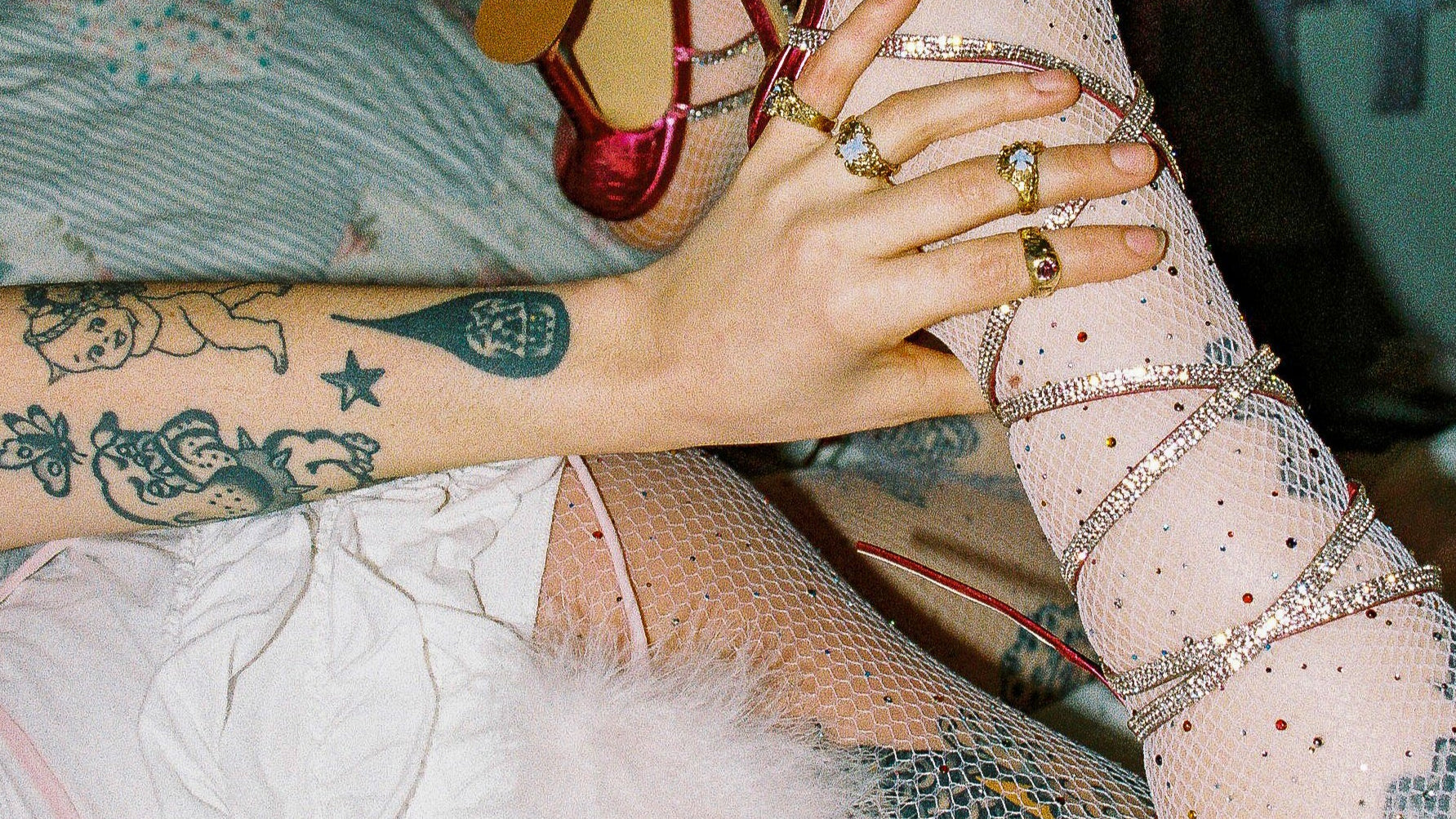 Close up of hand wearing multiple Metal Bones Jewellery rings and tattoos, styled with diamante red lace up heels and fishnet stockings