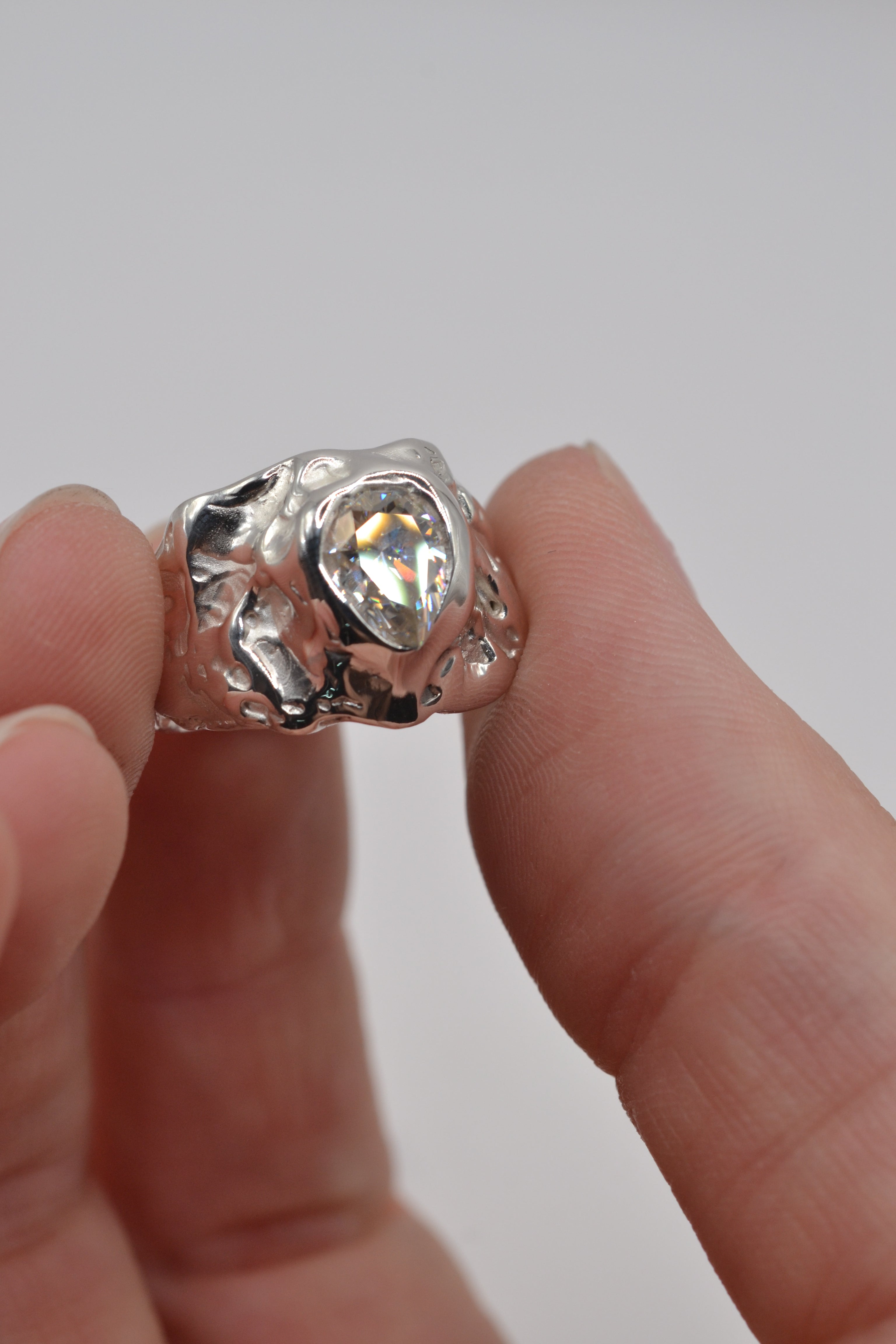 Lost wax cast silver Molten Memory Ring held in hand sculptural alternative engagement ring with pear cut moissanite and organic silver setting
