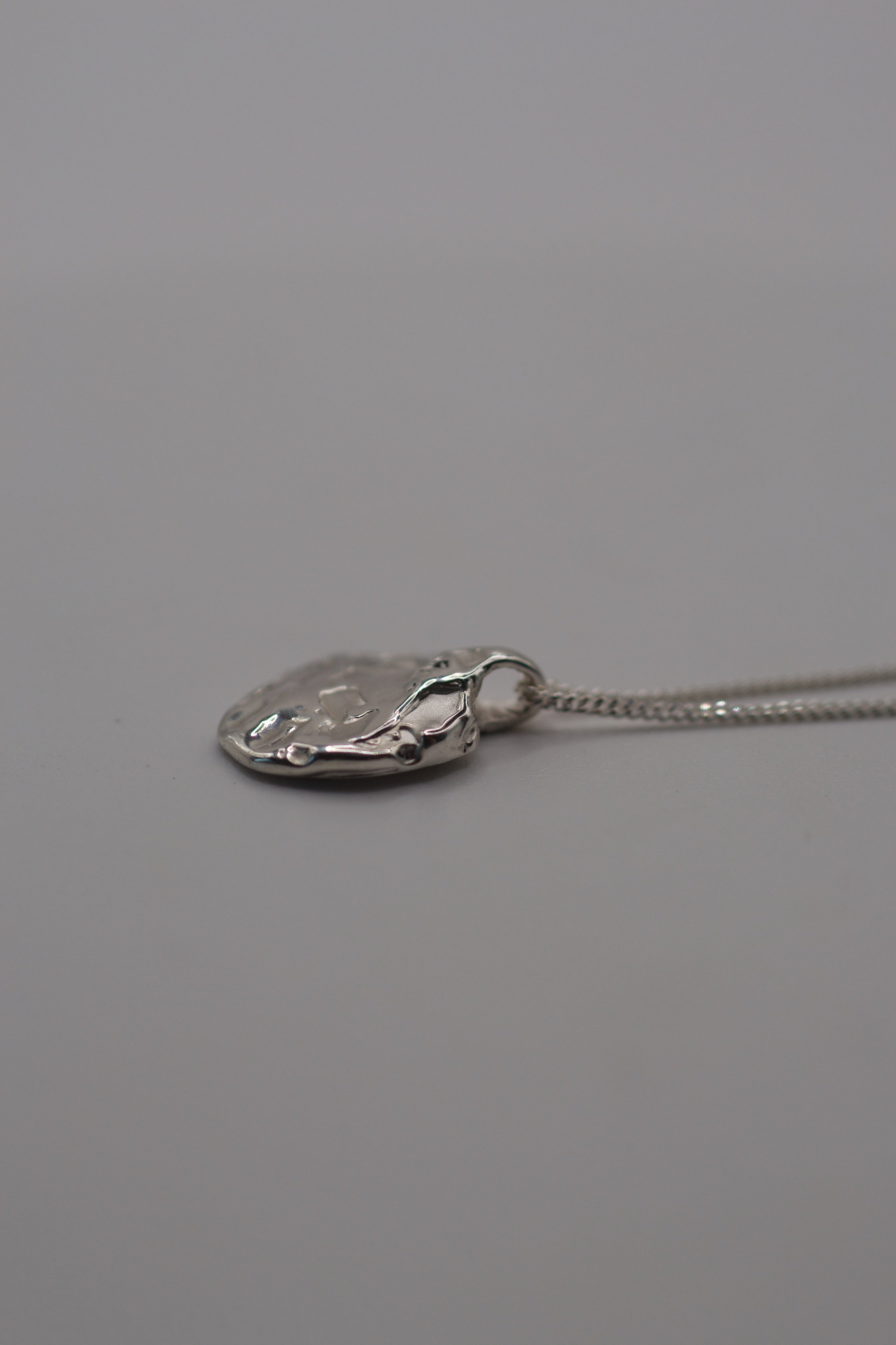 Flat lay of the Molten Pendant showing organic sculptural sterling silver form and soft molten texture handmade using lost wax casting