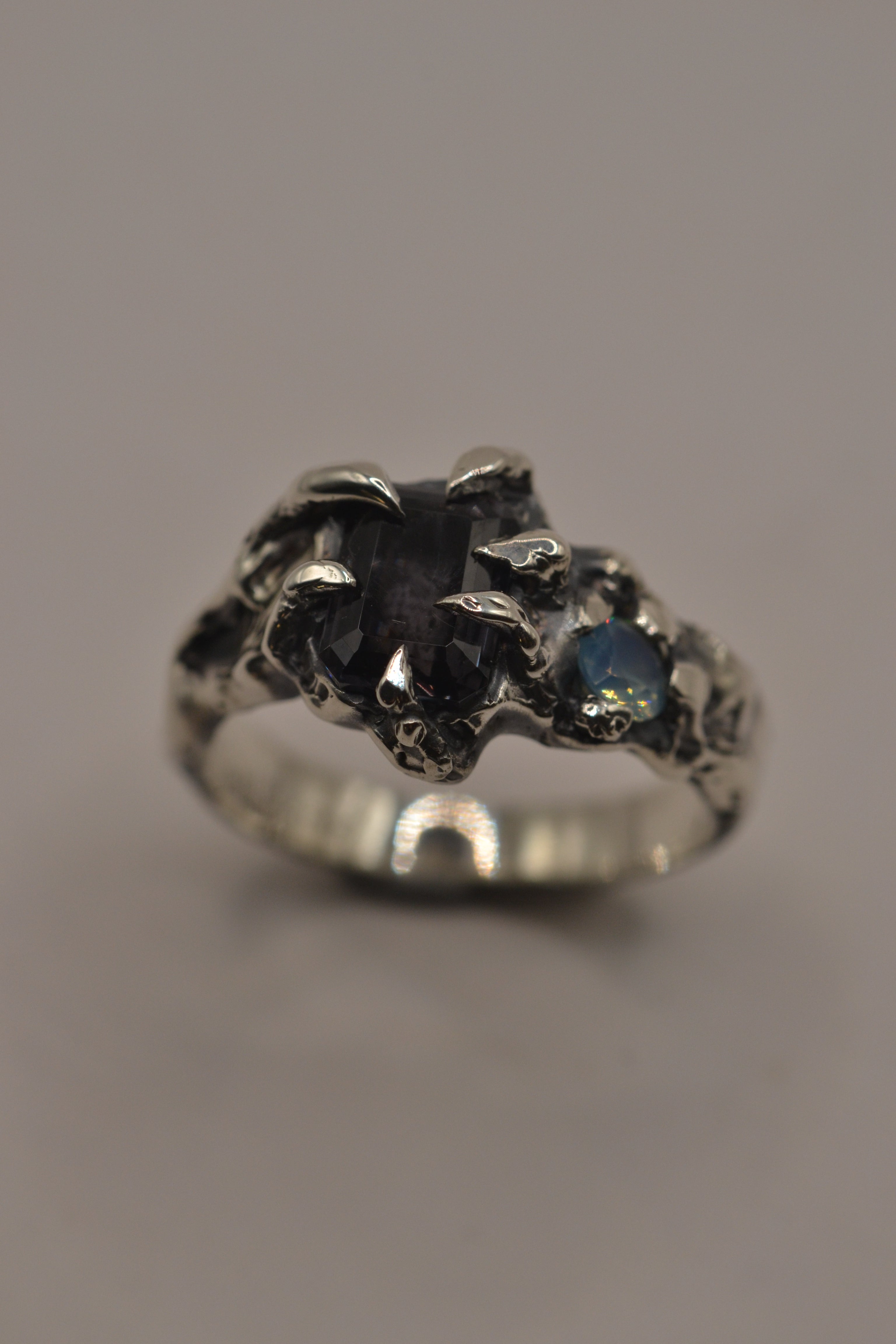 Front view of the Silhouette Ring showing milky aqua opal and grey spinel within six sculptural darkened sterling silver claws lost wax cast