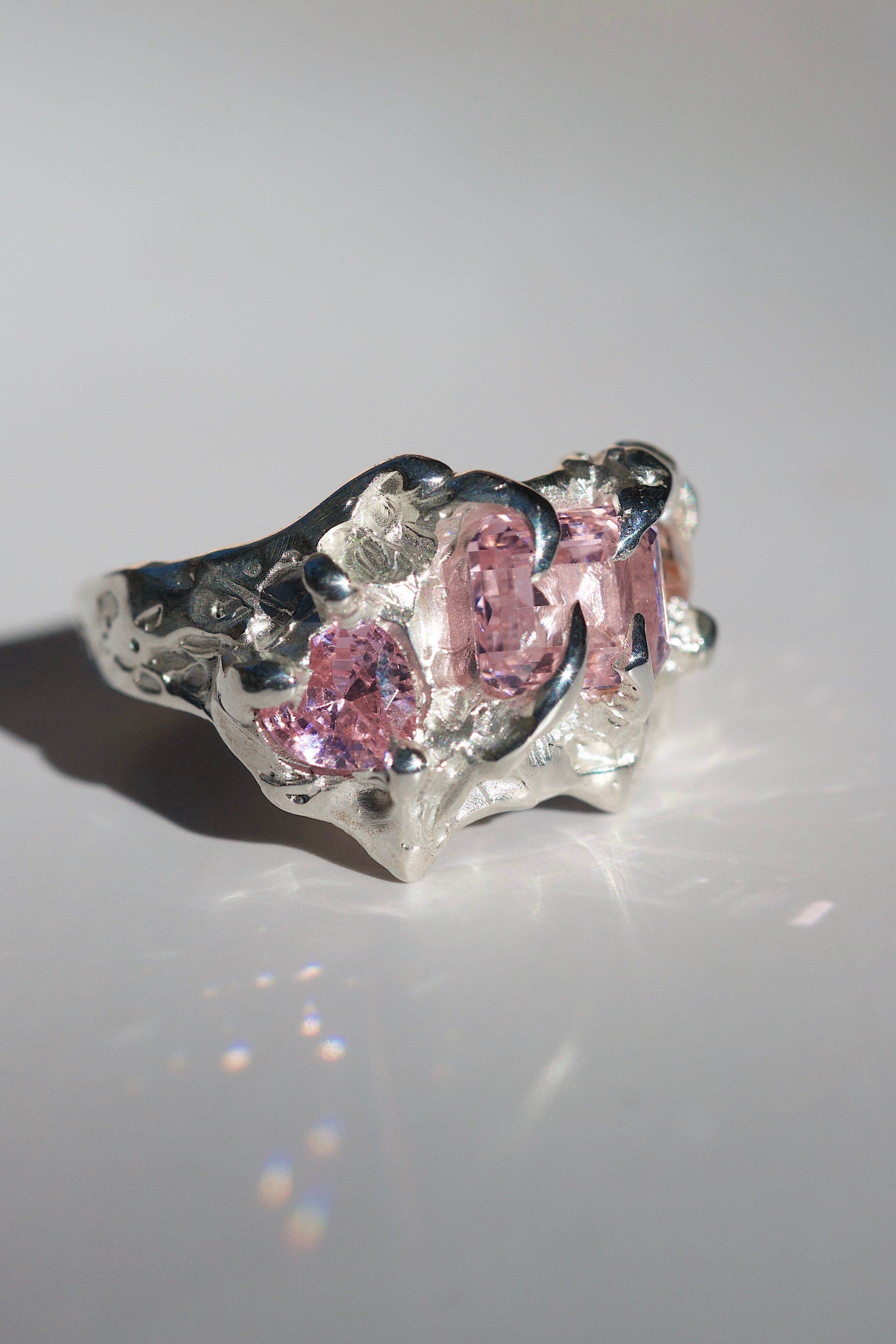 Silver molten ring ring with pink heart gemstones on a light gray background