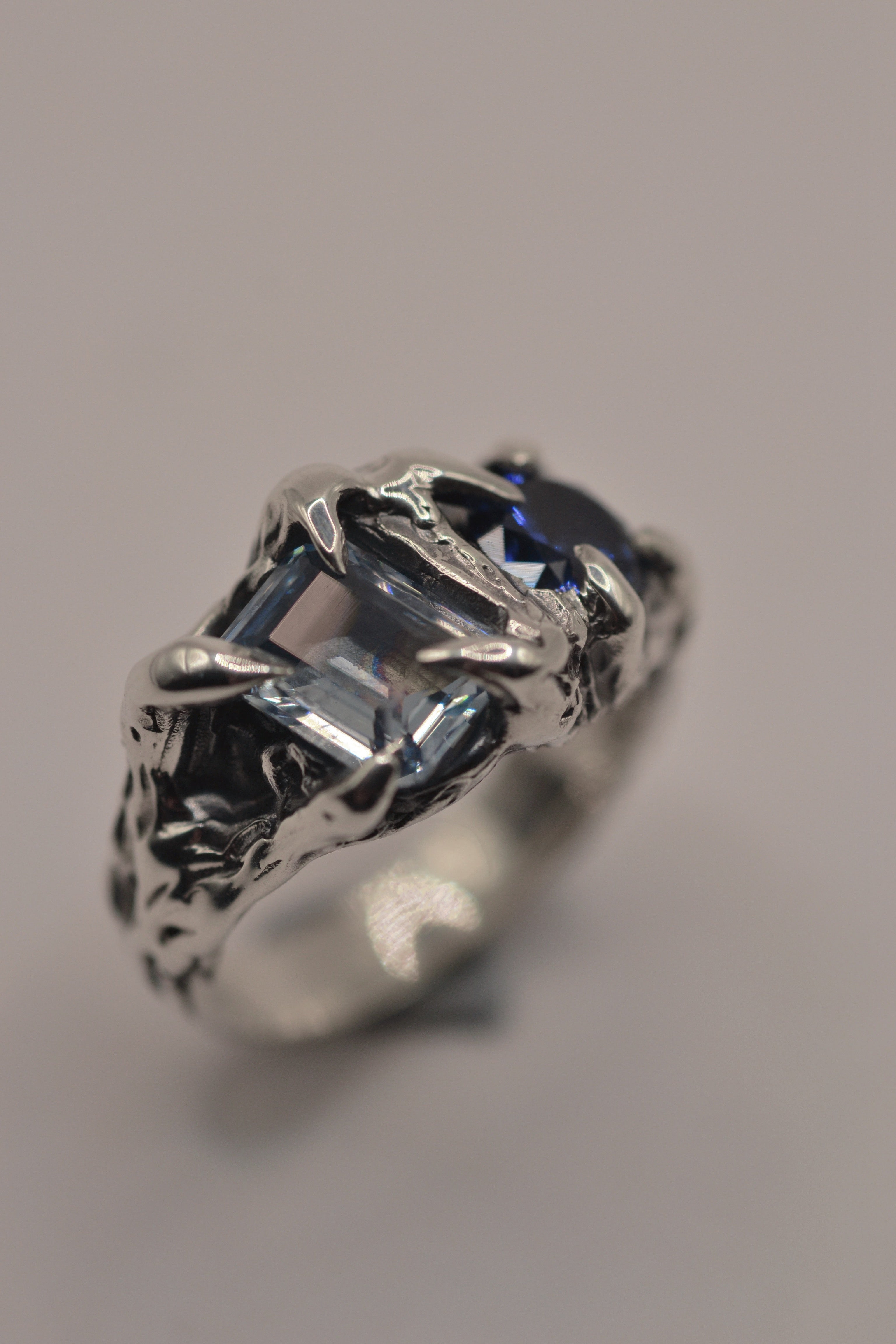 Handmade lost wax cast sterling silver ring with natural blue sapphire and lab-grown pale blue topaz set within dimensional textured darkened silver, gothic alternative ring made using the wax carving technique