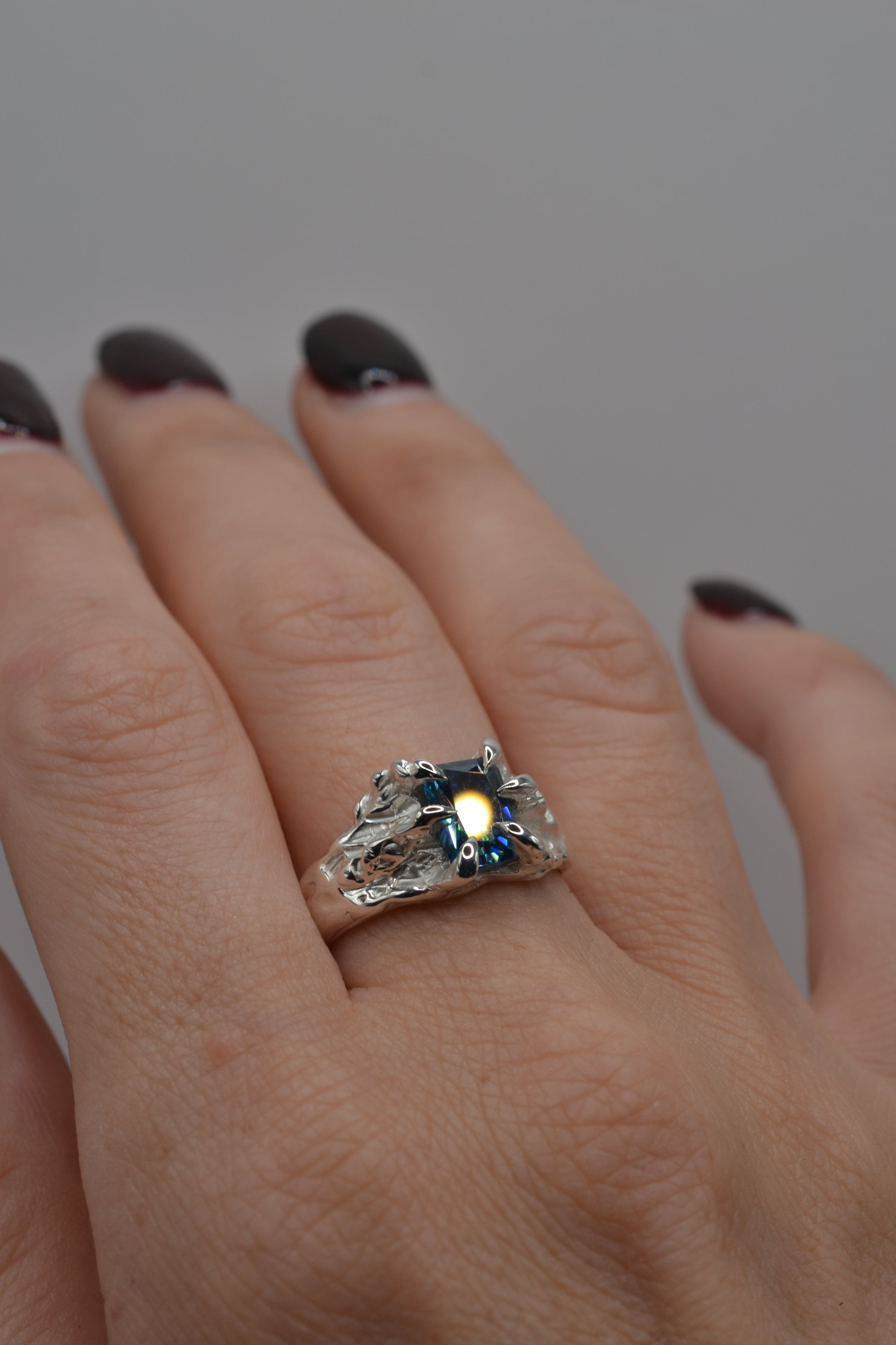 Lost wax cast silver Starburst Ring worn on hand non traditional engagement ring with blue moissanite and sculptural molten silver claws