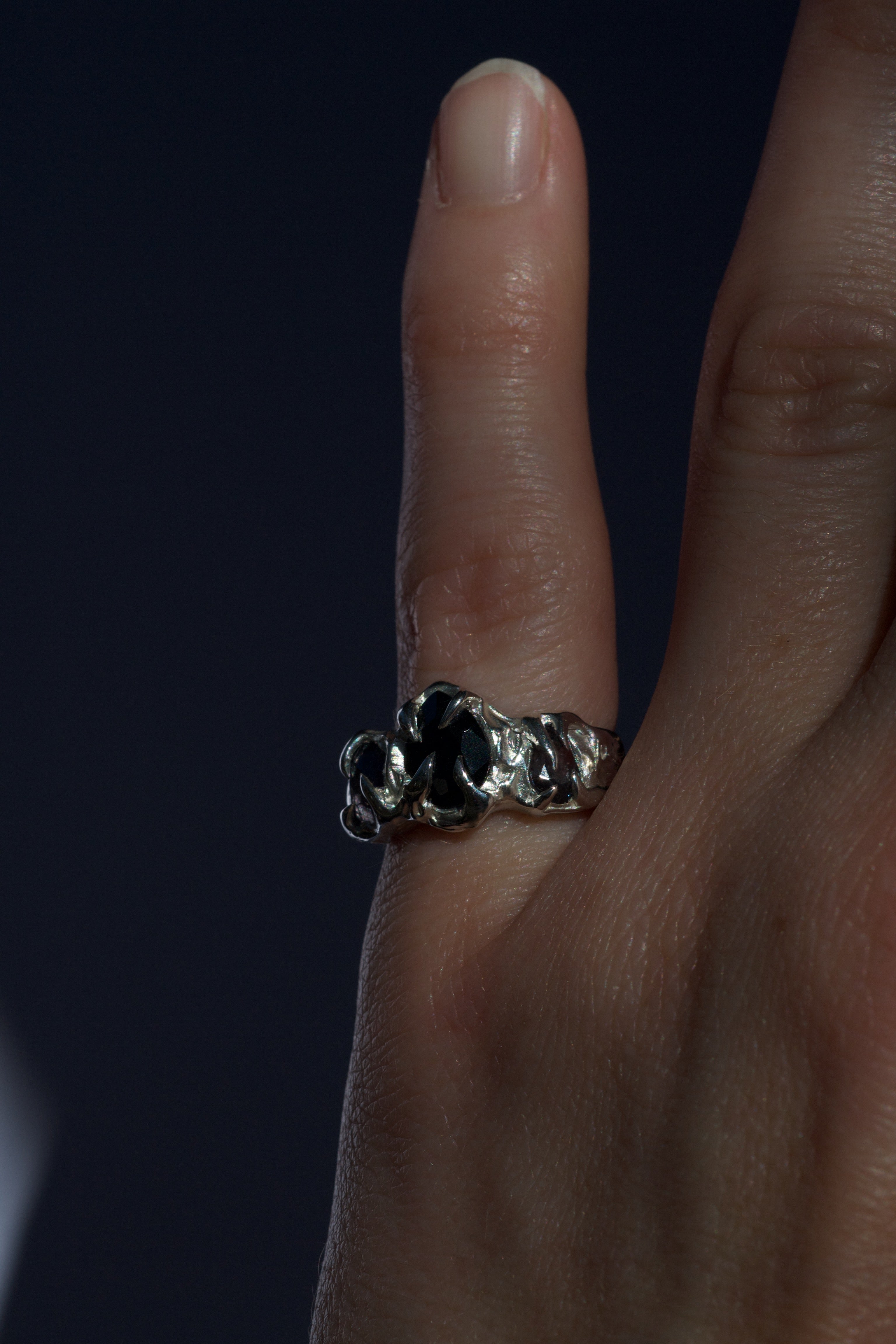 Womans pinky finger wearing a textured handmade lost wax ring with black pear-cut gemstones held in place by talon prongs.