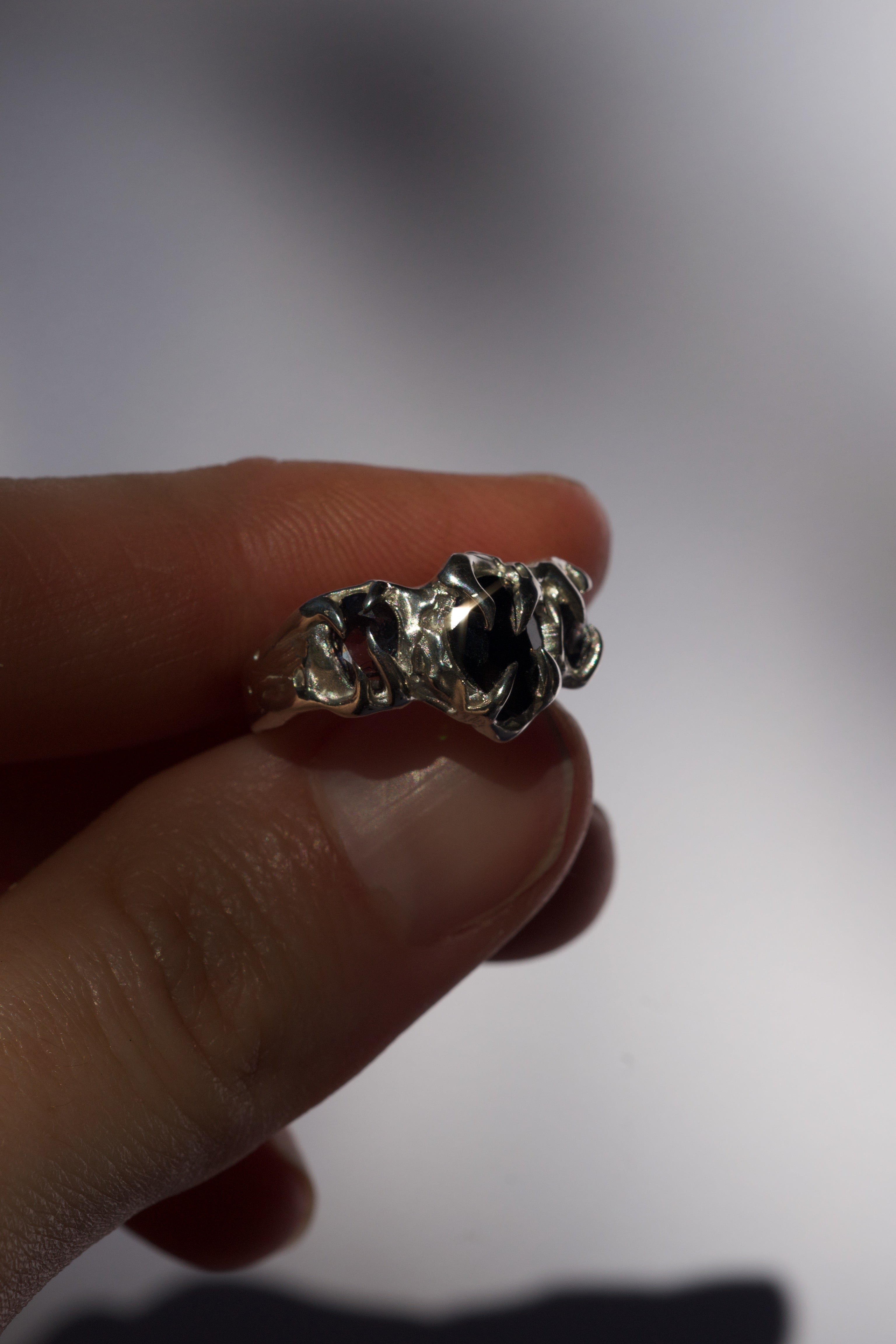Close up image of a sterling silver ring with black pear-cut lab-grown gemstones wedged between two fingers.