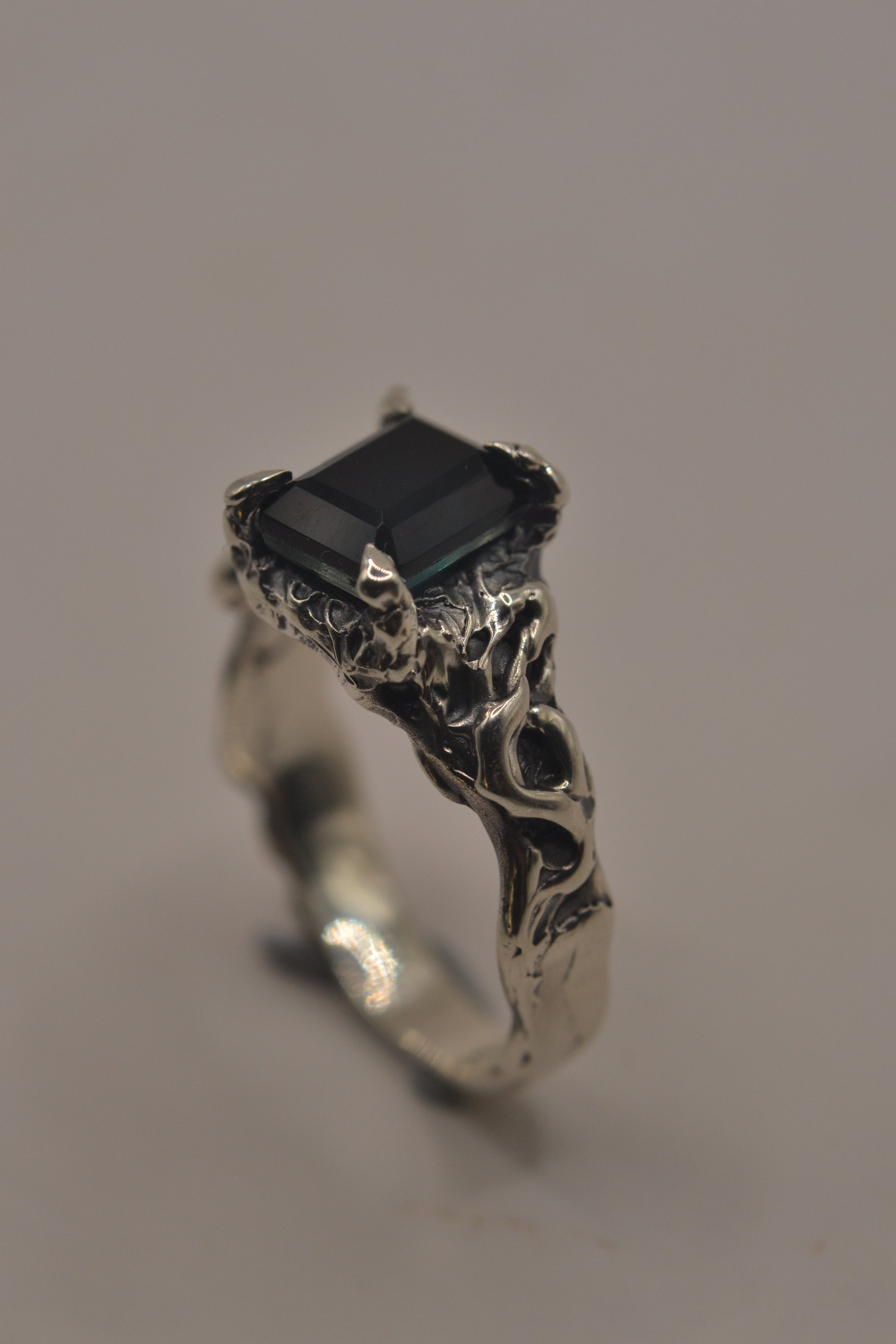 Macro photo of the Twilight Ring showing teal emerald cut sapphire and heavily textured darkened recycled sterling silver band