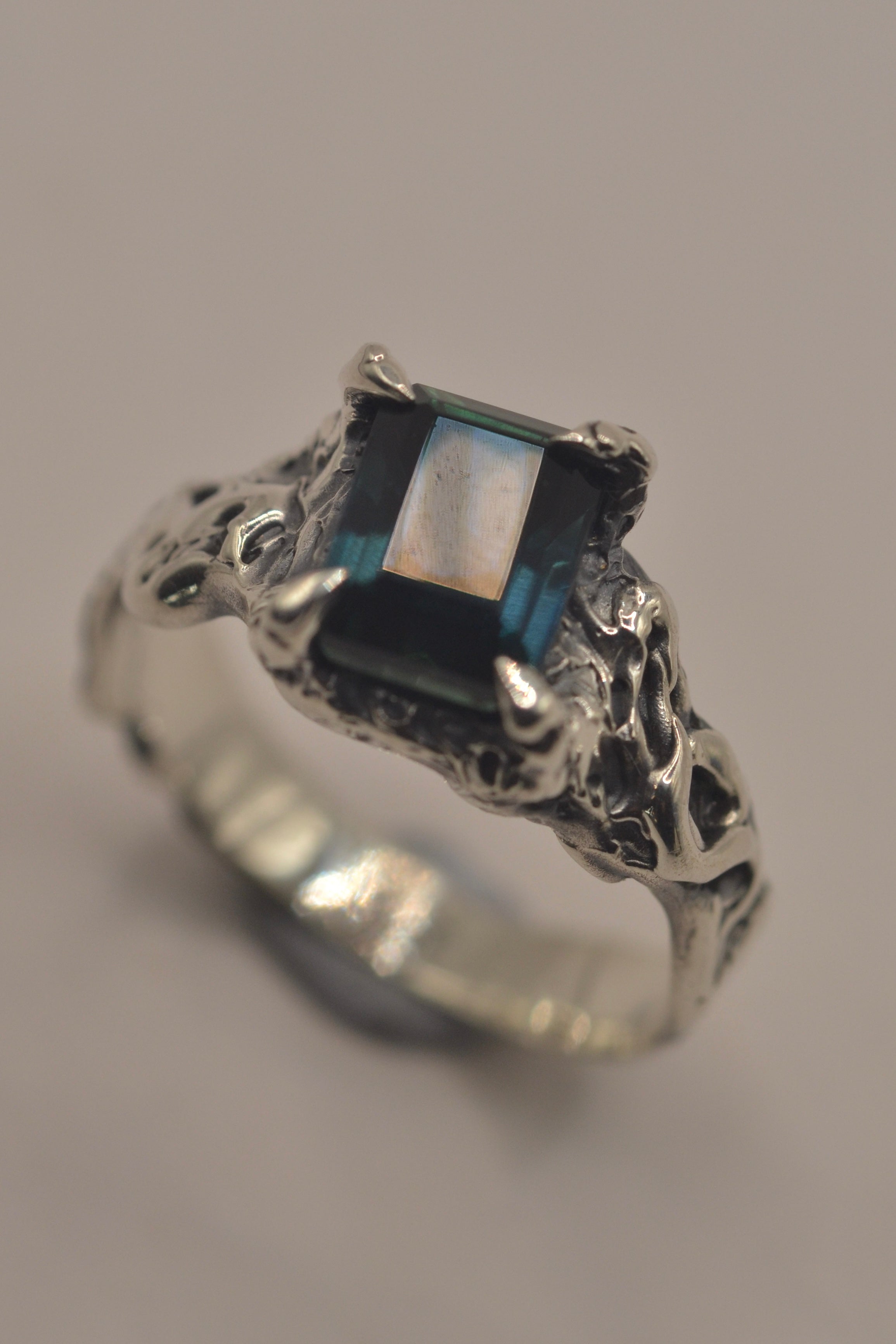 Handmade lost wax cast sterling silver ring with teal emerald cut lab-grown sapphire set within heavily textured darkened silver, gothic inspired statement ring made using the wax carving technique