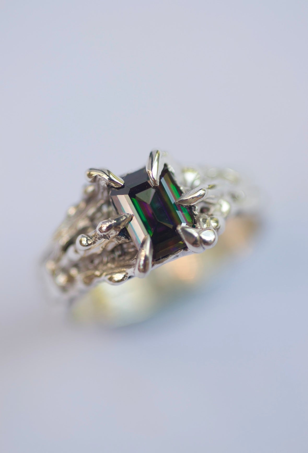 Handmade lost wax cast sterling silver ring with sharp molten dragon-style claws gripping a vibrant rainbow emerald cut moissanite, bold mystical alternative ring made using the wax carving technique