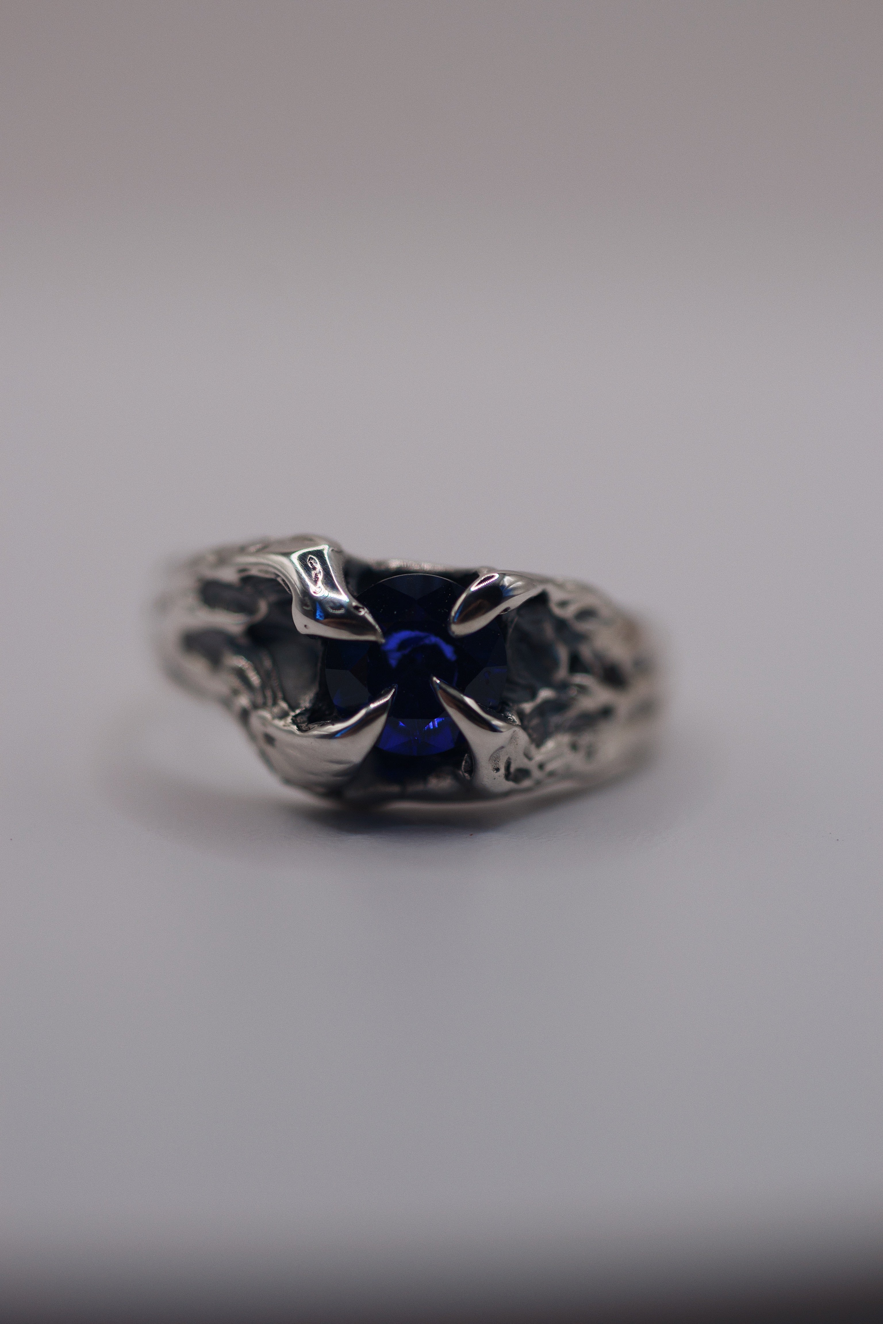 Front view of the Volcanic Ring showing deep blue natural sapphire within four darkened molten sterling silver claws handmade using lost wax casting