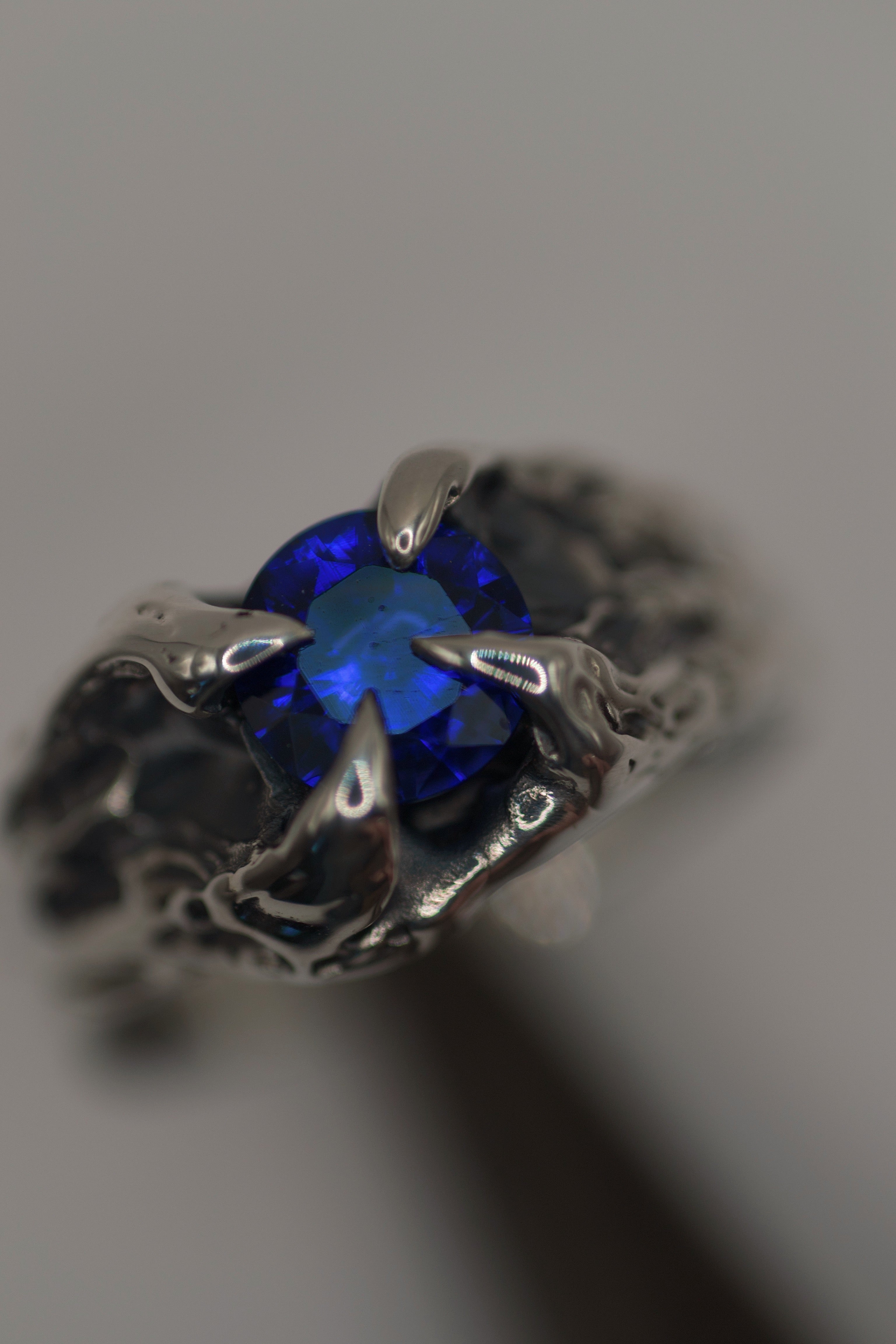 Handmade lost wax cast sterling silver ring with four darkened molten claws gripping a deep blue natural sapphire, powerful alternative ring made using the wax carving technique