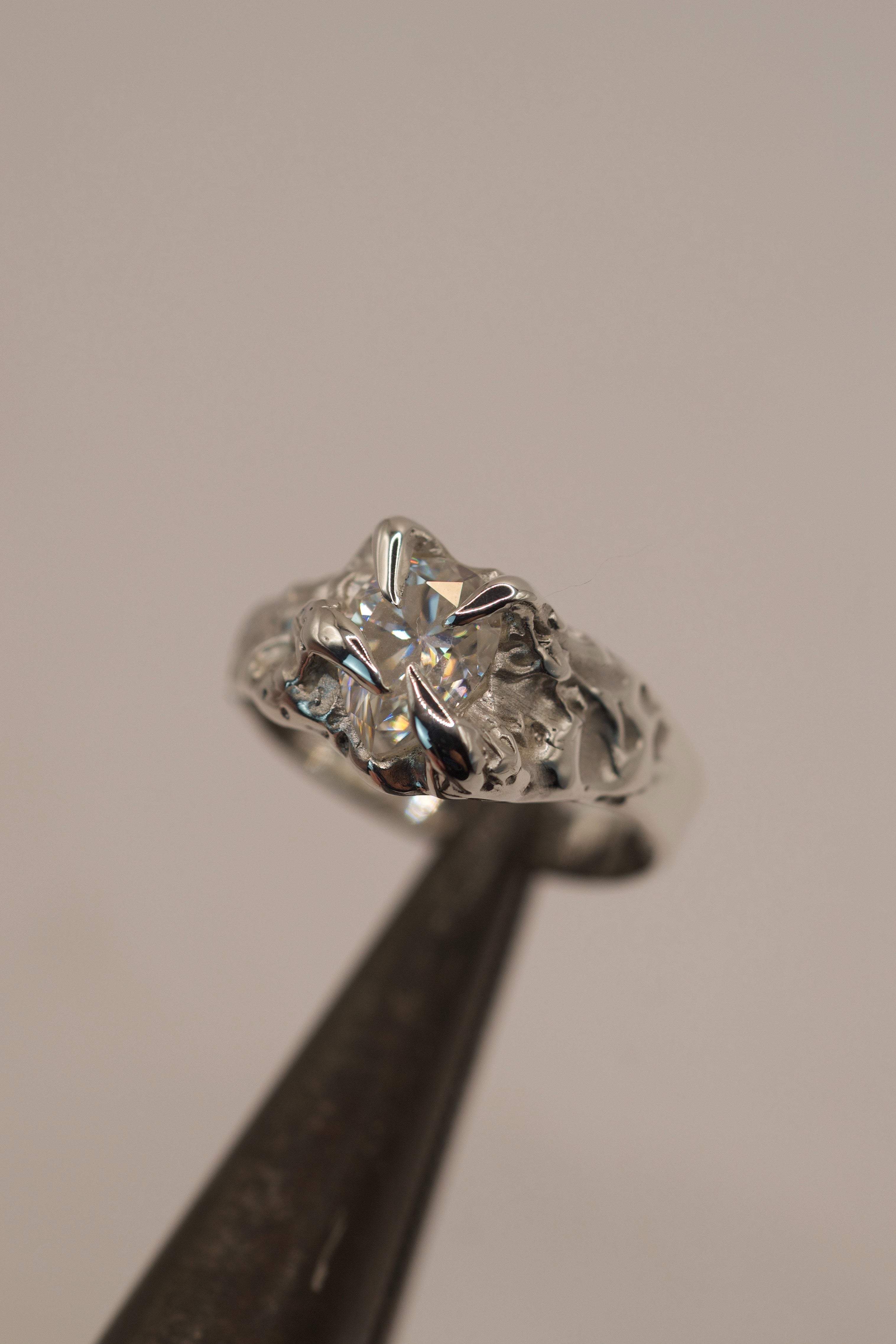 Top down angle of the Winter Ring in tweezers showing luminous pear cut moissanite and organic icy molten silver setting handmade using lost wax casting