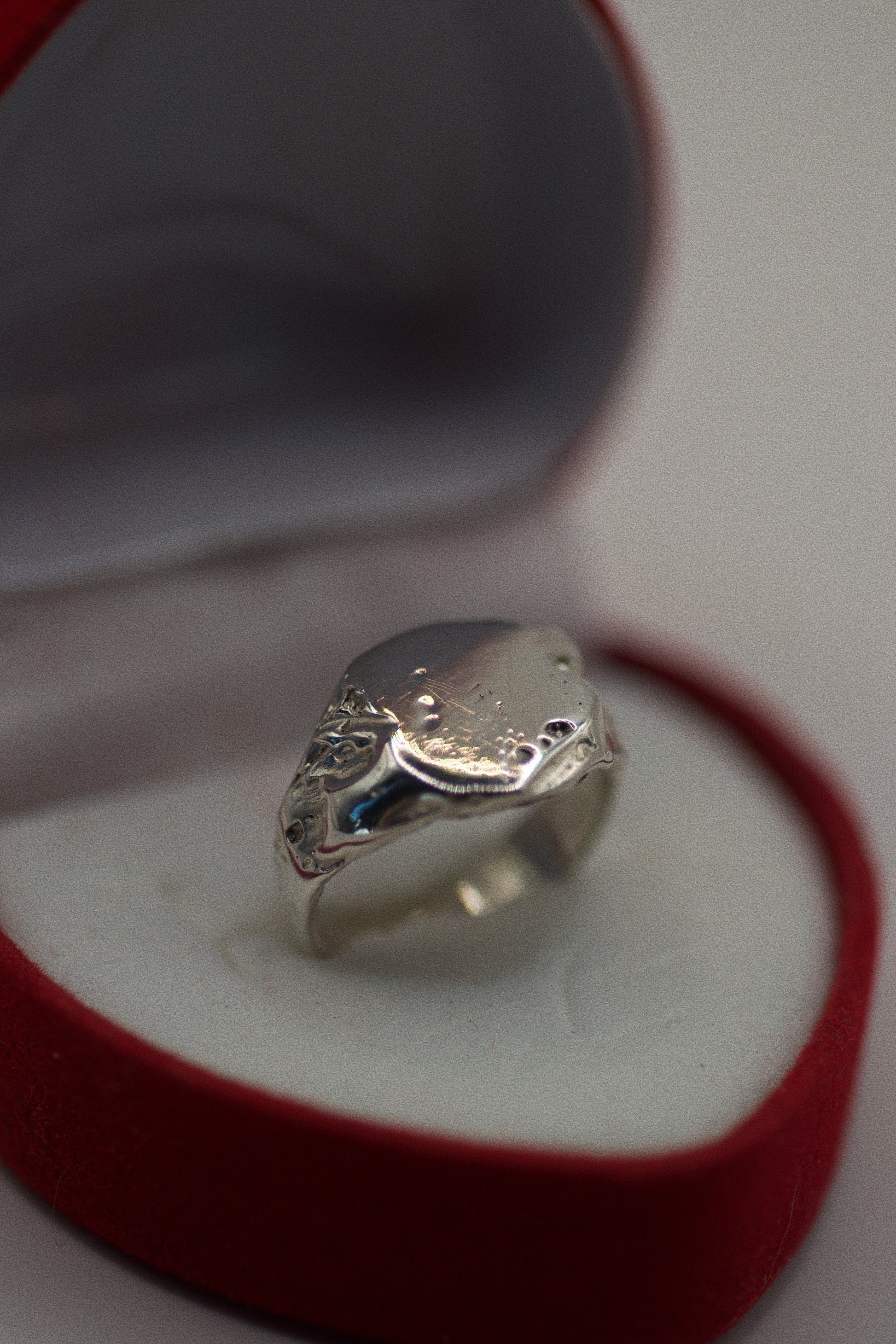 This 925 sterling silver signet ring is crafted with an organic, textured surface that features natural dips, grooves, and imperfections. The band is smooth and sleek, contrasting with the rougher, sculpted areas that create a rugged, earthy aesthetic. The ring’s flat surface has craters and subtle indentations, enhancing its unique, handmade look. Created using the lost wax method, this ring is as much a piece of art as it is a bold, wearable accessory.