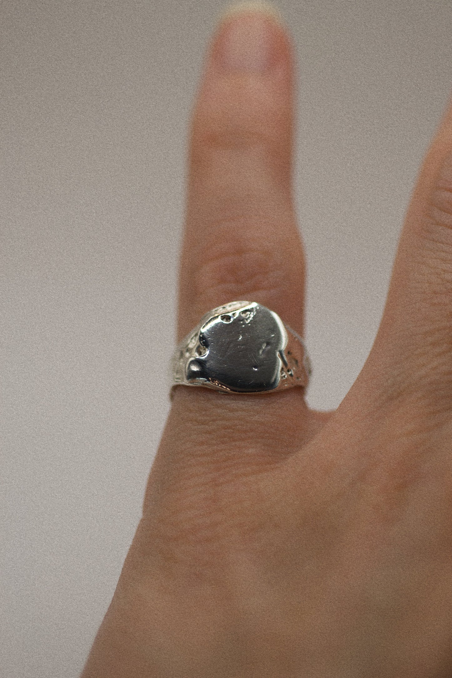 This 925 sterling silver signet ring has an organic, sculpted texture, with dips and grooves that create a rugged, earthy feel. The flat surface of the ring features slight craters, adding character and depth to its sleek band. The contrasting smooth and textured areas give the ring an elegant yet raw aesthetic. Made using the lost wax method, this ring is a testament to the art of handcrafted silver.