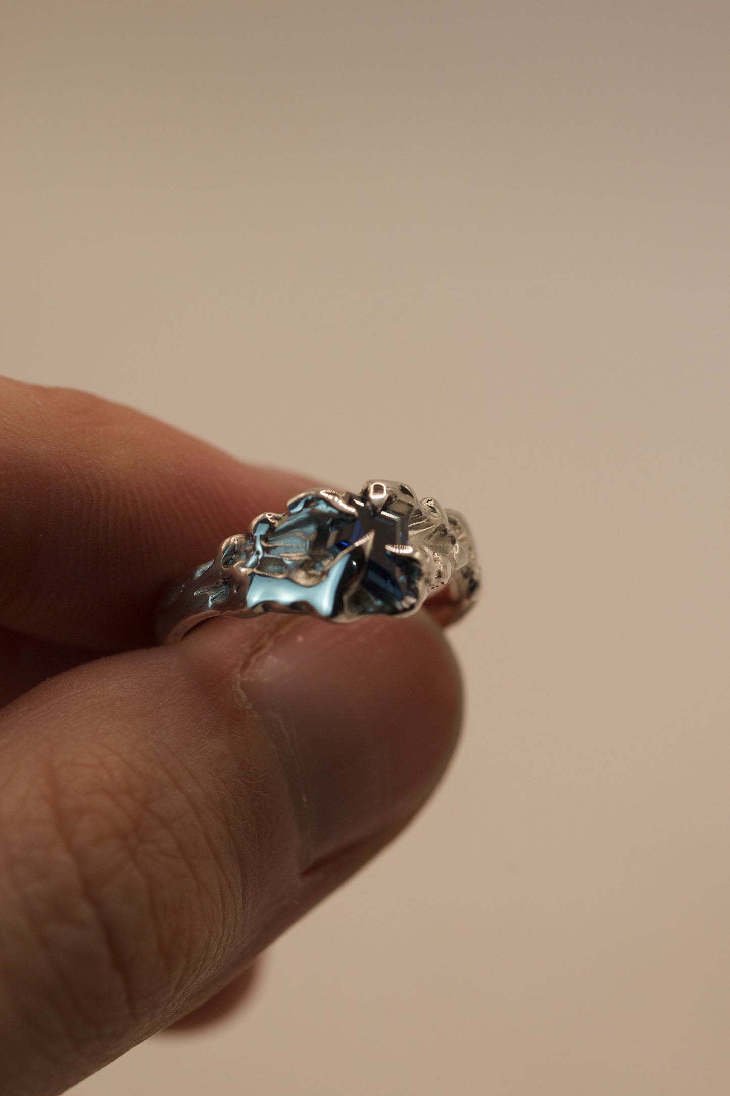 This asymmetrical sterling silver ring was handmade with the lost wax technique, featuring organic molten textures and gothic inspired claws around a vivid blue kite cut moissanite stone.