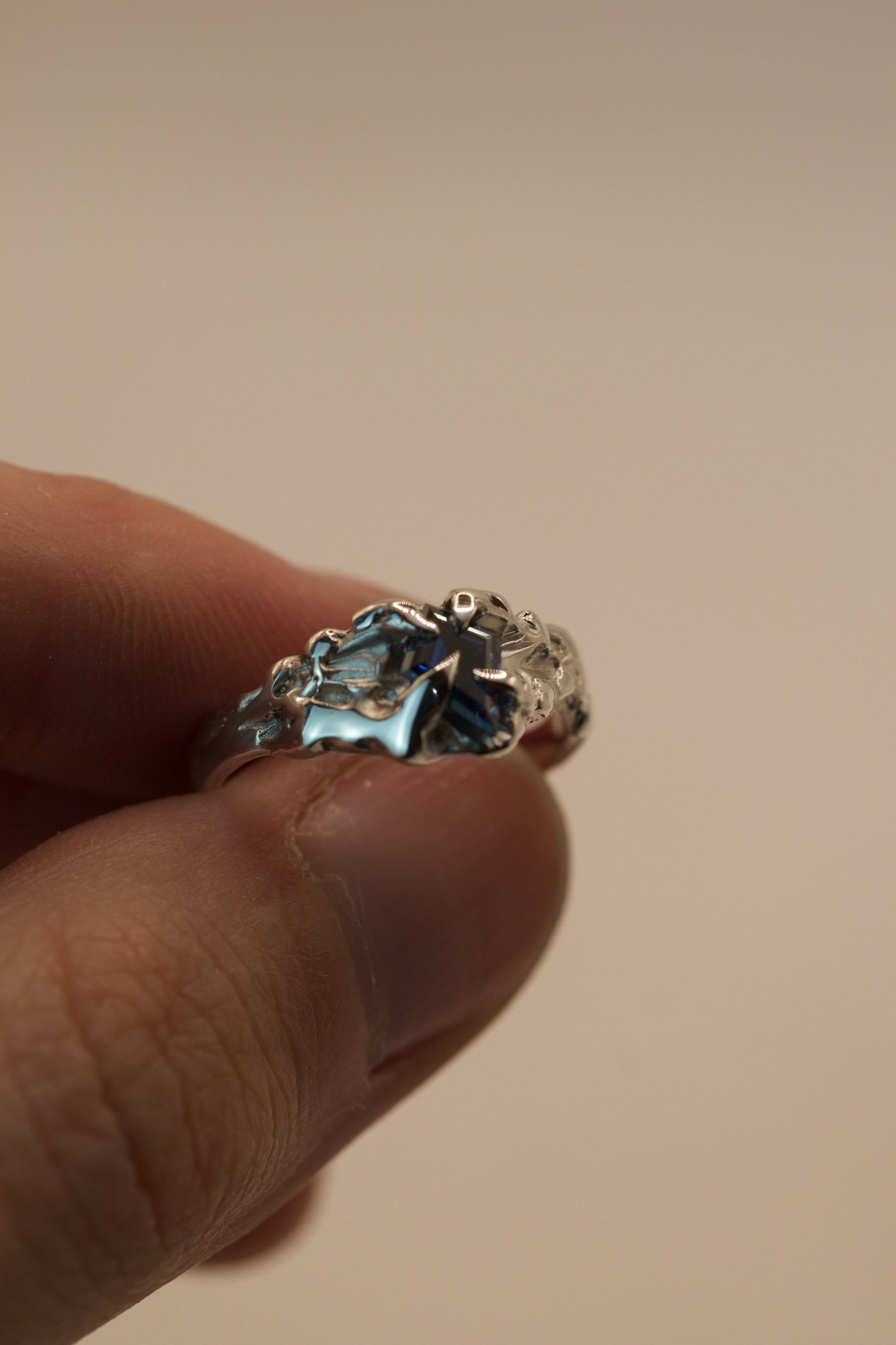 This asymmetrical sterling silver ring was handmade with the lost wax technique, featuring organic molten textures and gothic inspired claws around a vivid blue kite cut moissanite stone.