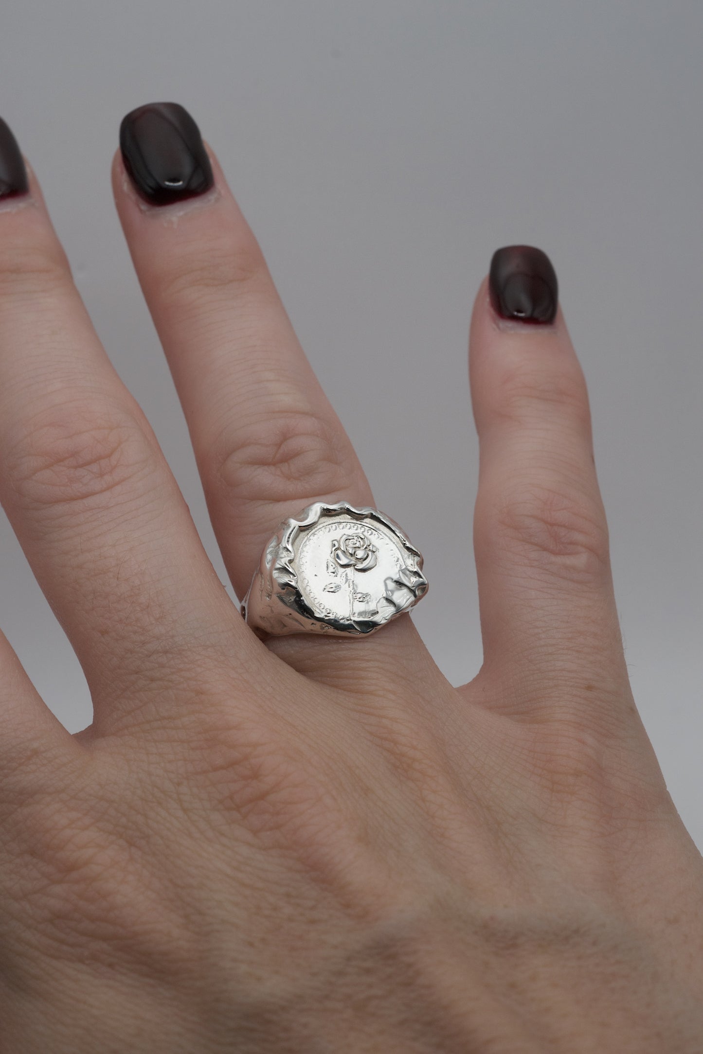 Alternative gothic style silver signet ring with a raised rose design and molten texture, handmade using lost wax casting and worn on the finger.