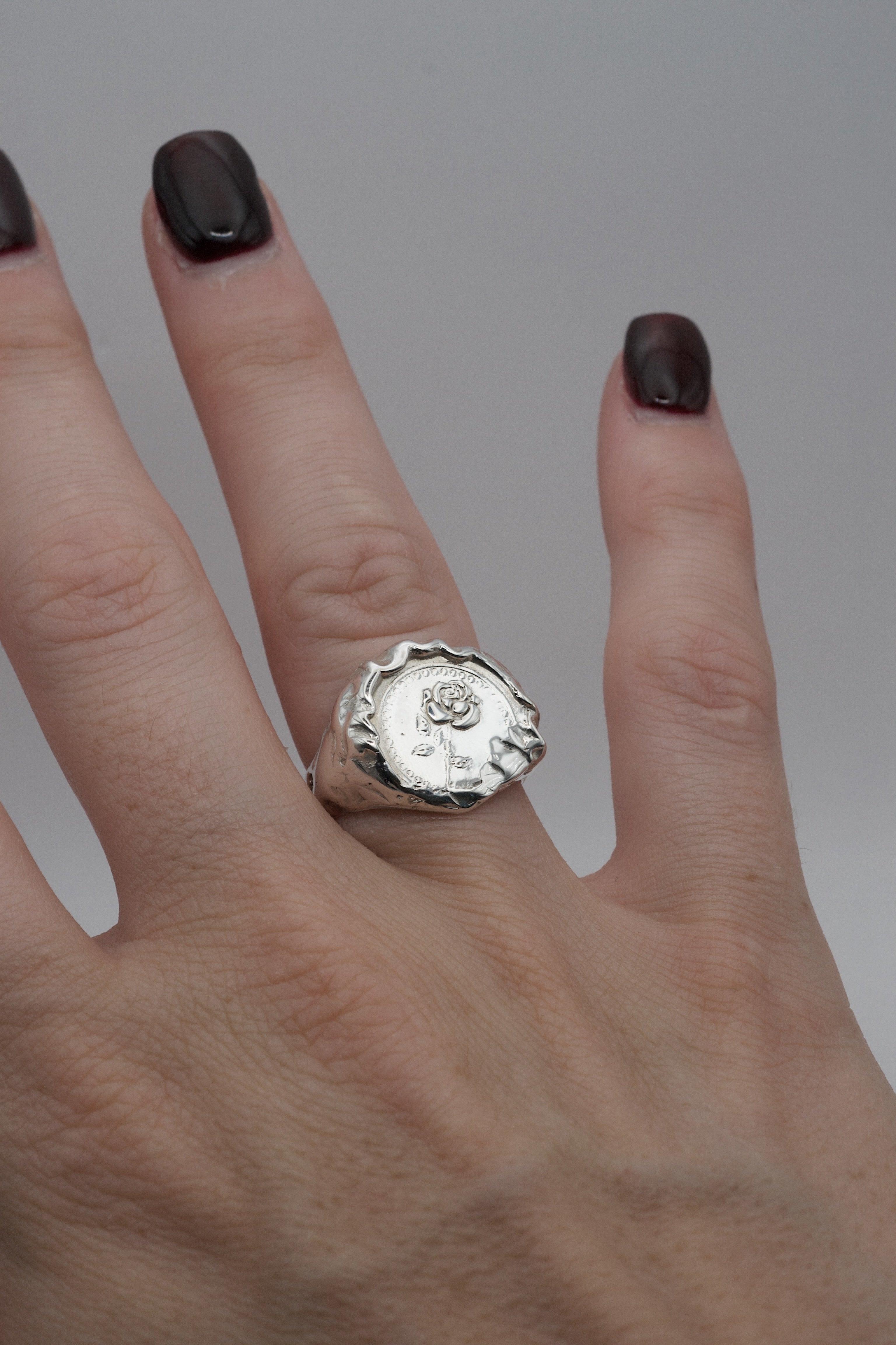 Alternative gothic style silver signet ring with a raised rose design and molten texture, handmade using lost wax casting and worn on the finger.