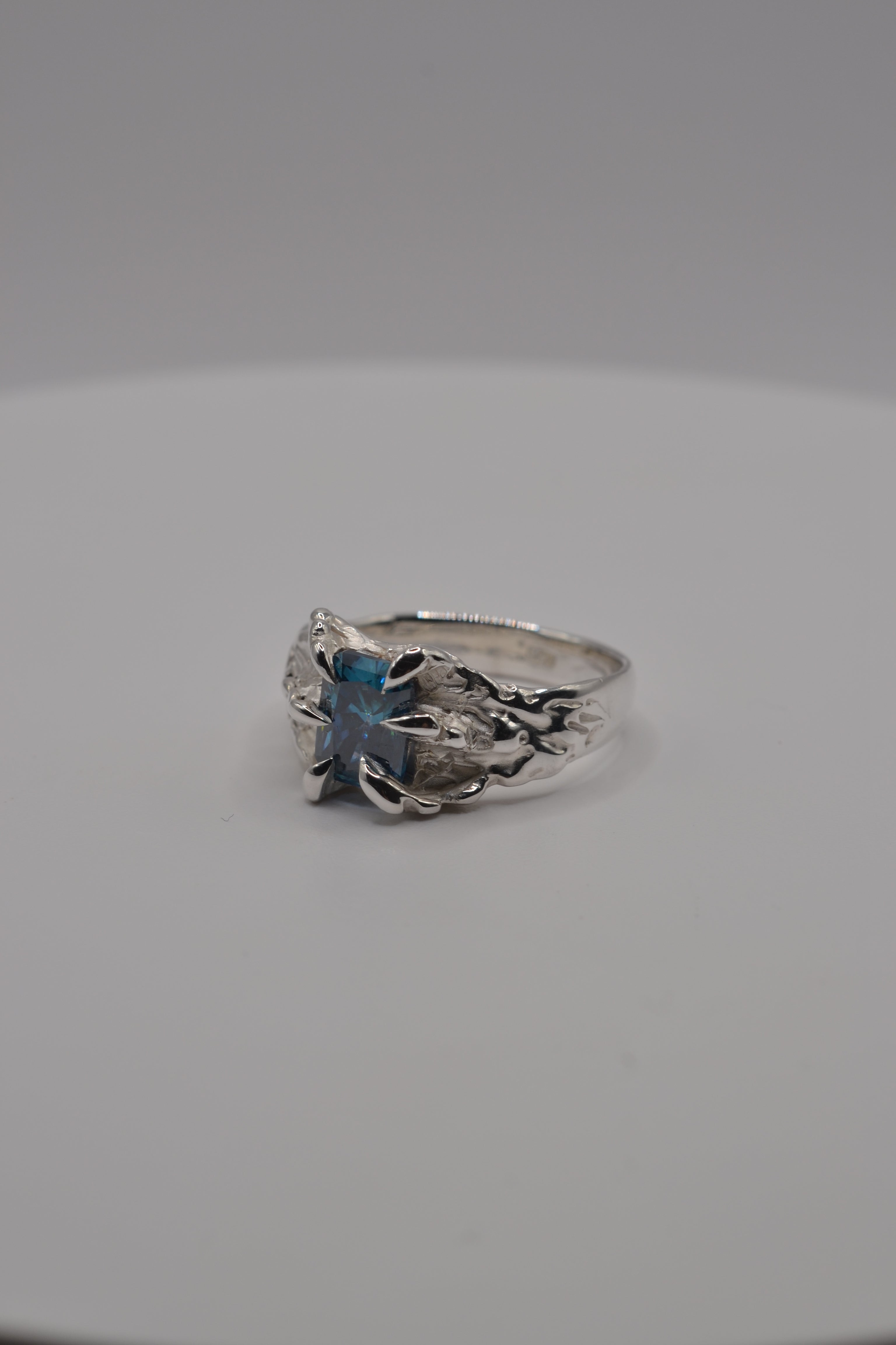 Angled side profile of a handcrafted alternative silver ring made using lost wax casting with a blue radiant cut moissanite.