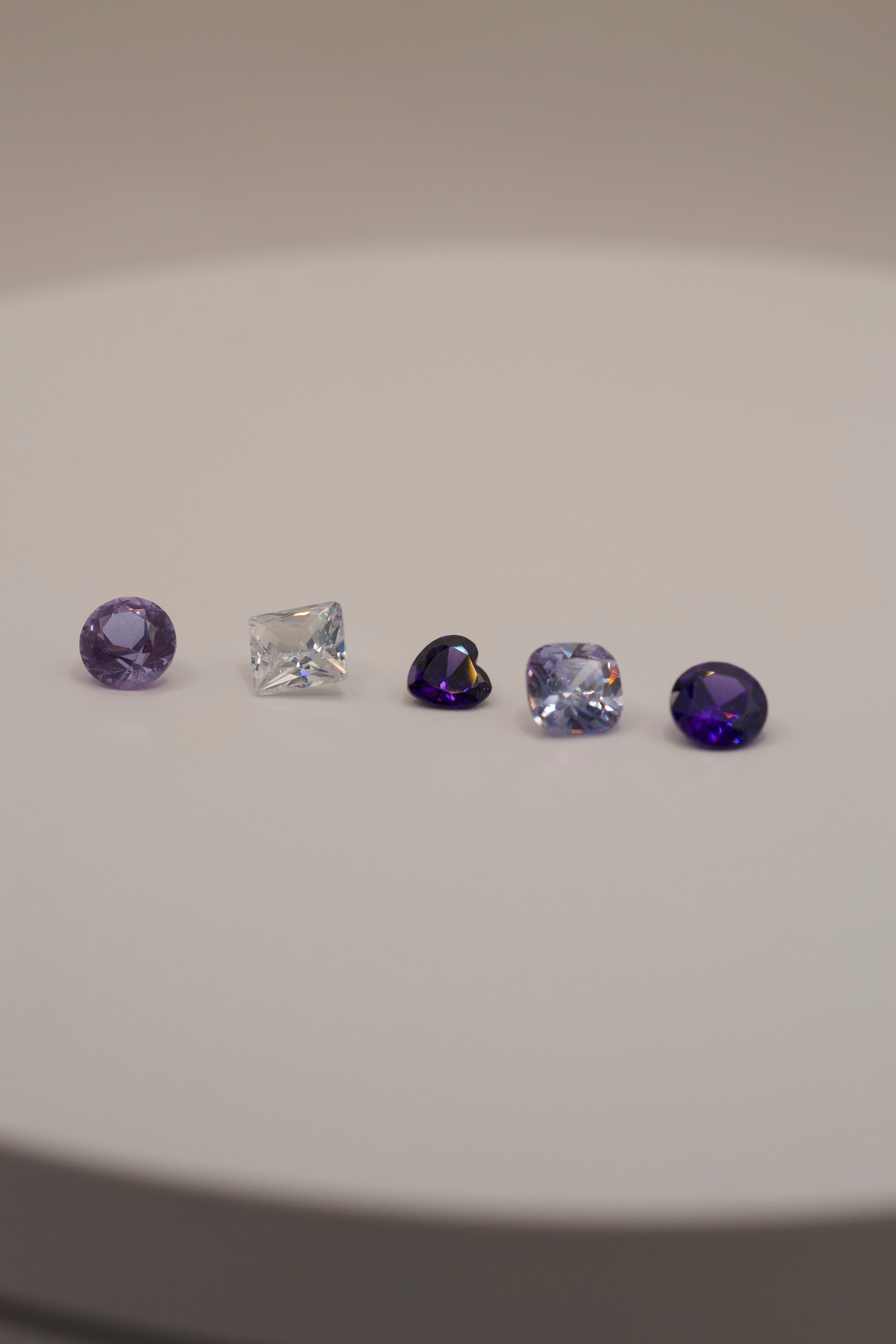 Faceted gemstones for lost wax casting in place, featuring violet, lavender, and clear stones in a variety of cuts for organic jewellery designs.