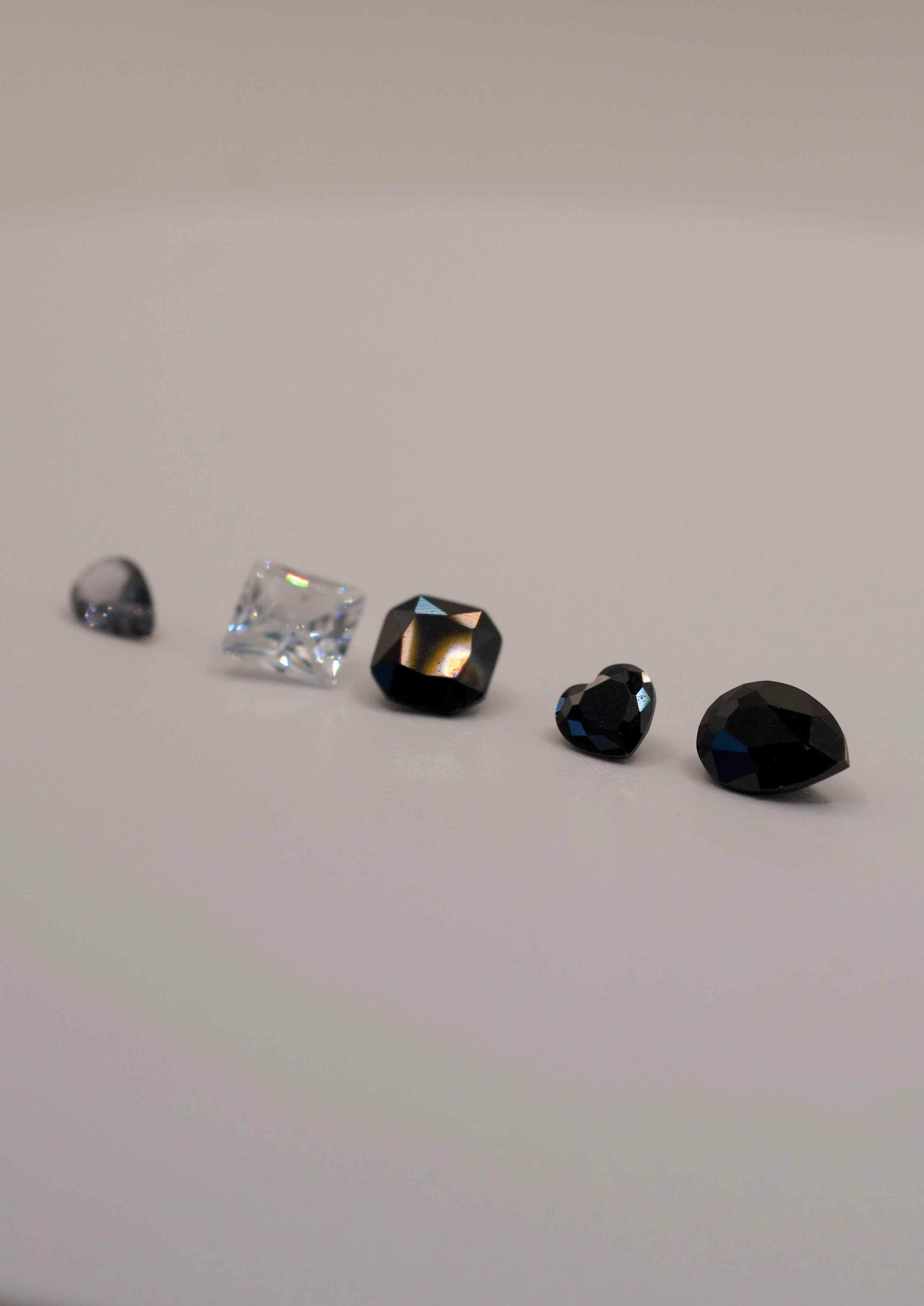 Assorted gemstones for wax carving and casting in place jewellery, including pear cut black, heart cut black, cushion black, clear princess cut, and teardrop stones.